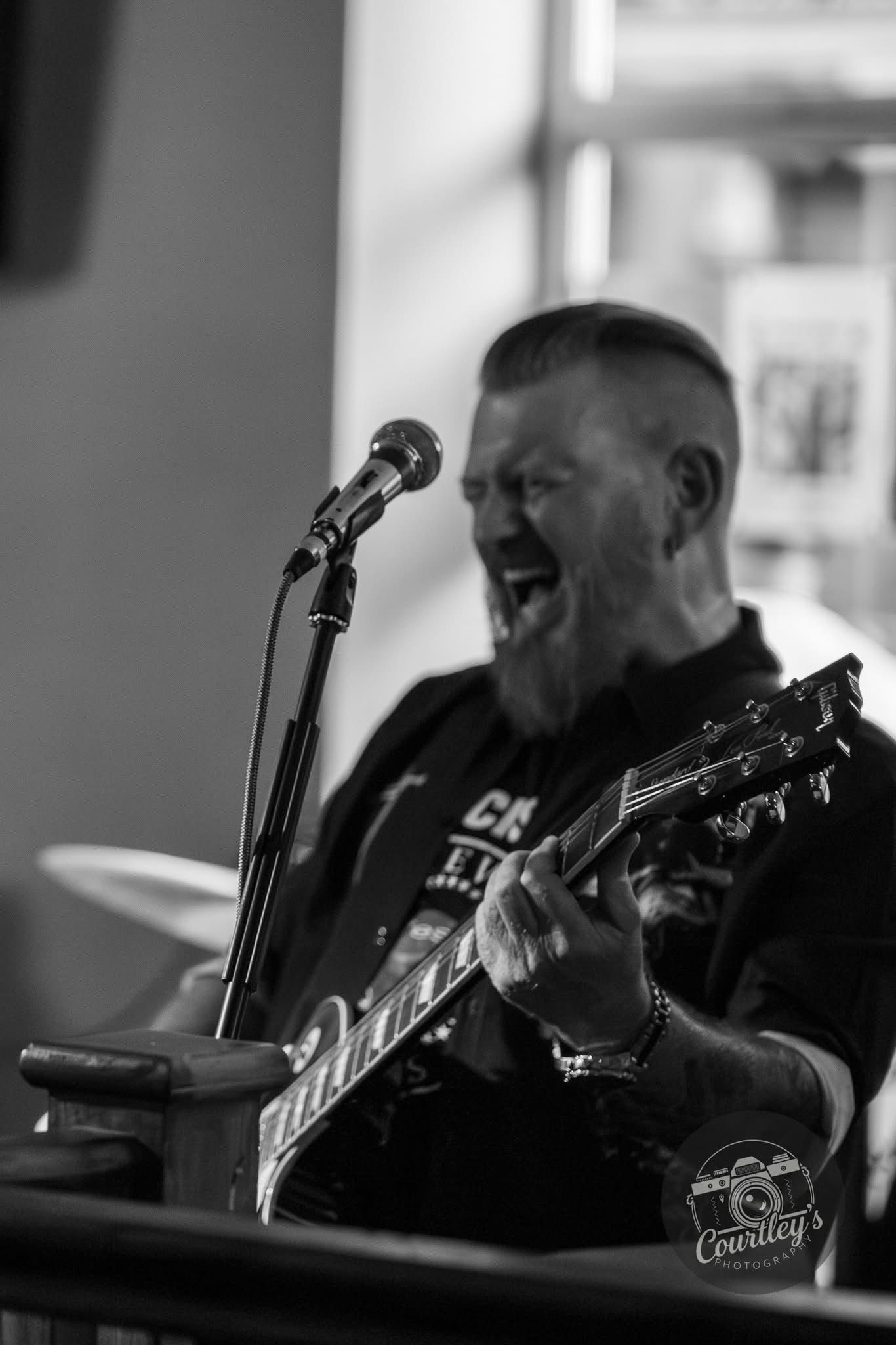 Guitarist with guitar singing into a microphone in black and white