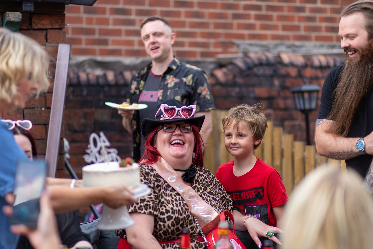 Friends and family smiling at an outdoor Birthday party with a cake