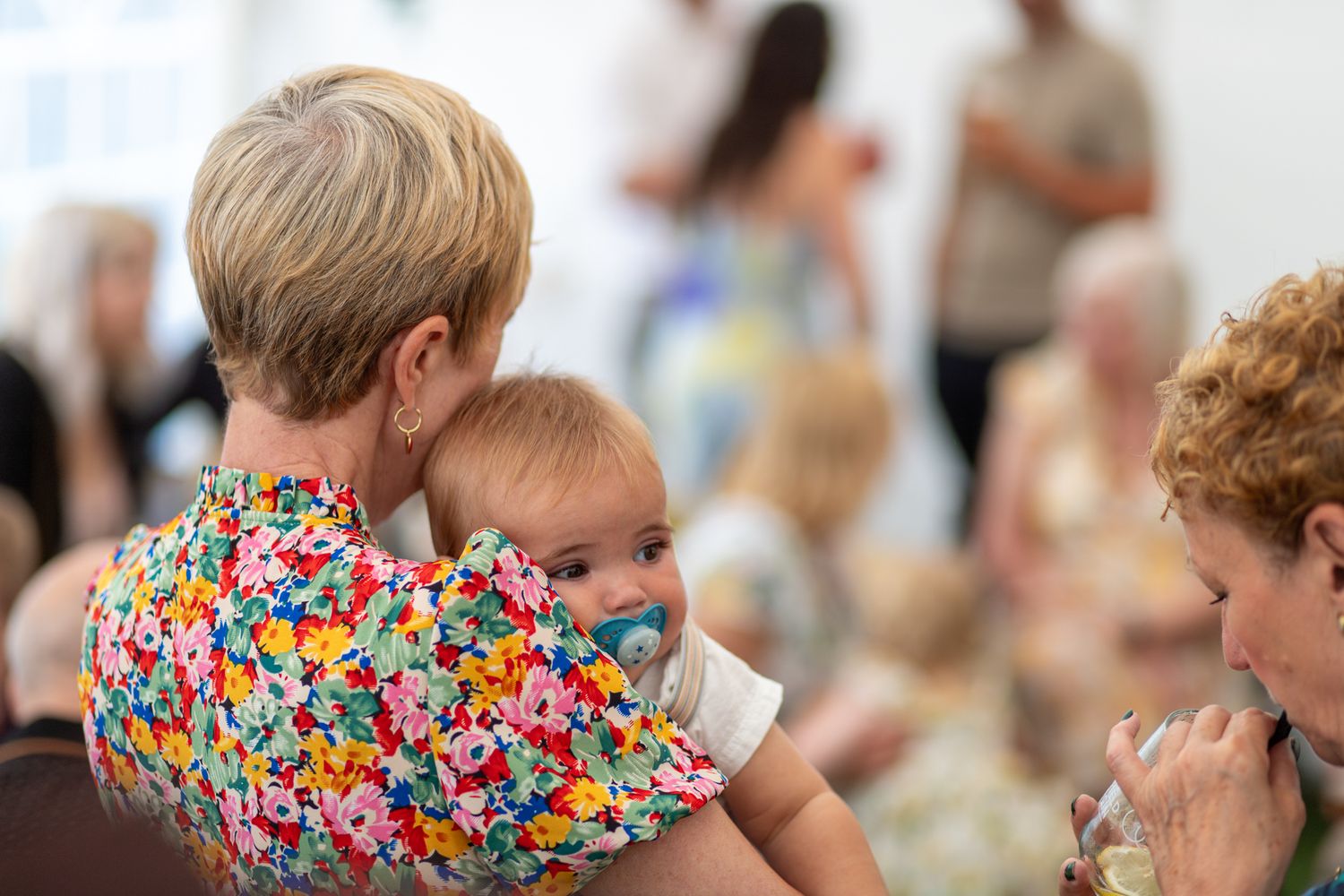 Woman in a floral dress holding a tired baby at an indoor Christening