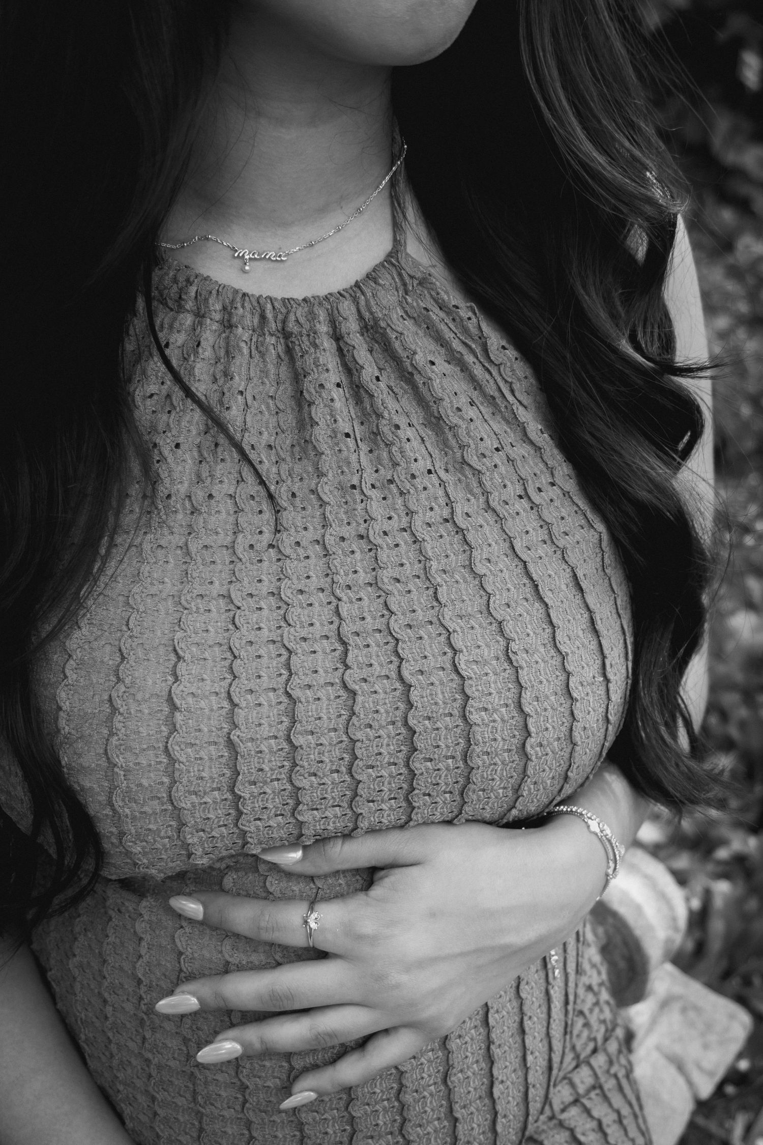 Black and white photo of someone wearing a knitted sweater with long dark hair and delicate necklace.