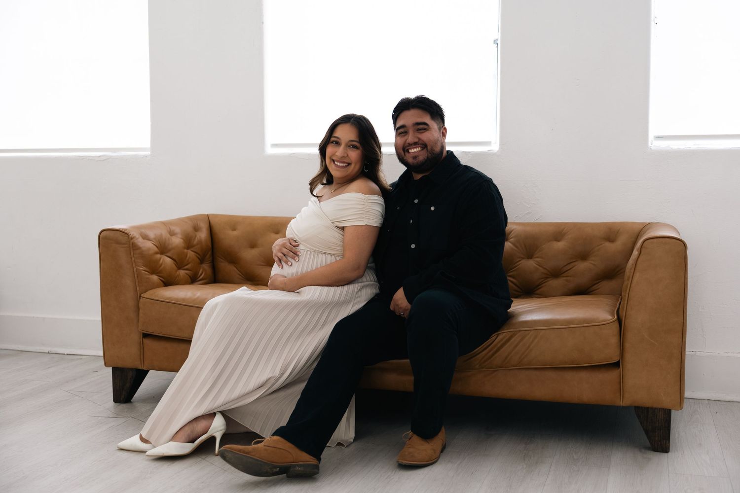 Two people sit together on a tan leather sofa in a bright, minimalist living room.