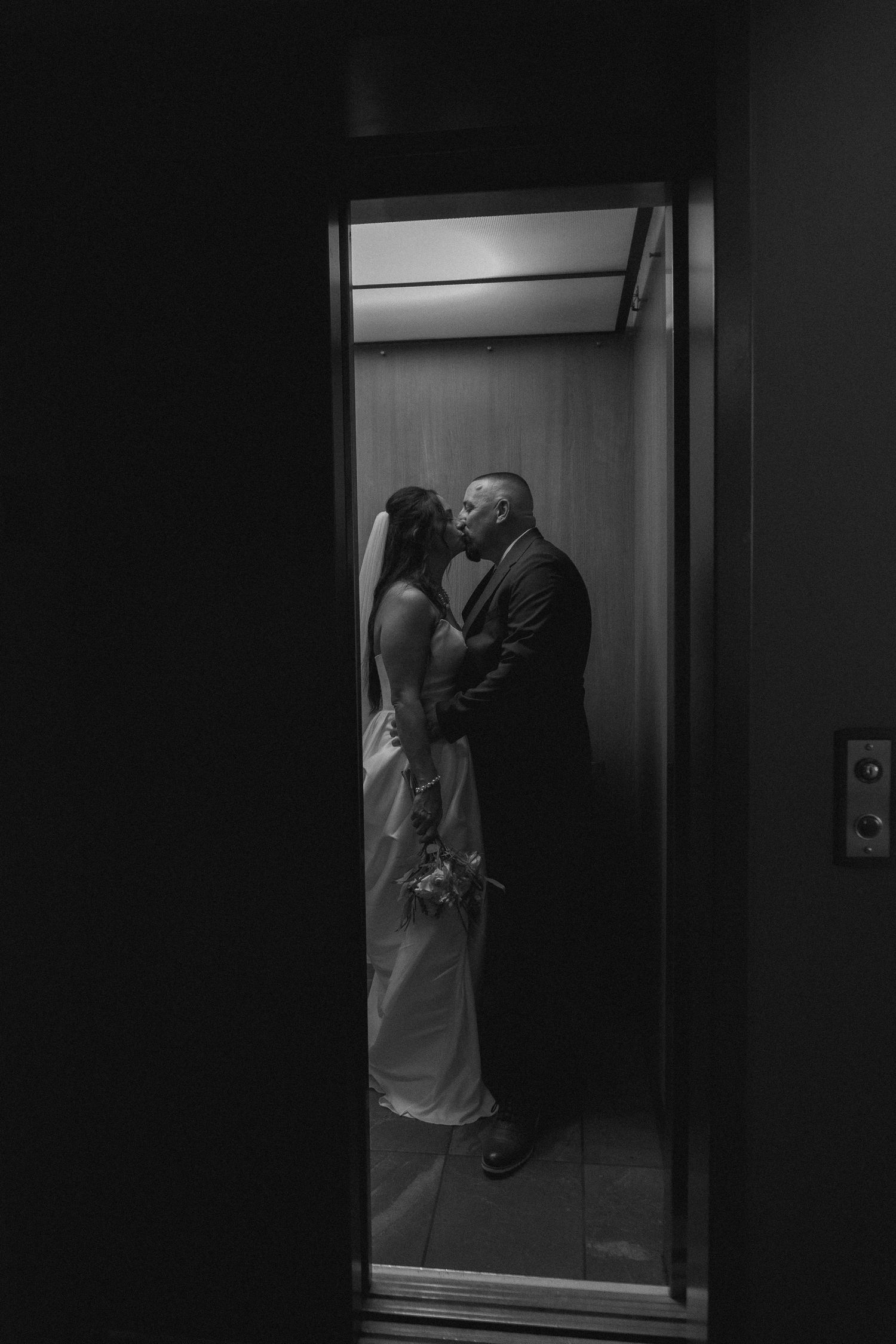 A romantic black and white photograph of a couple sharing an intimate moment in an elevator.