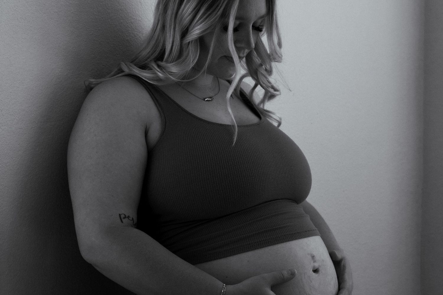Intimate maternity portrait in black and white showing pregnant belly in dark top.