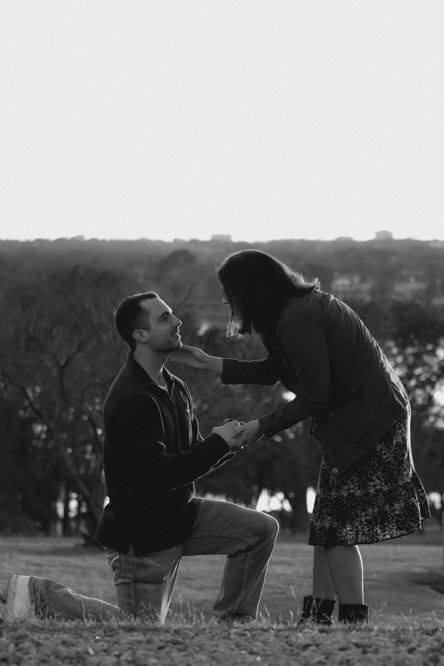 A proposal moment captured in silhouette against a scenic hillside backdrop.