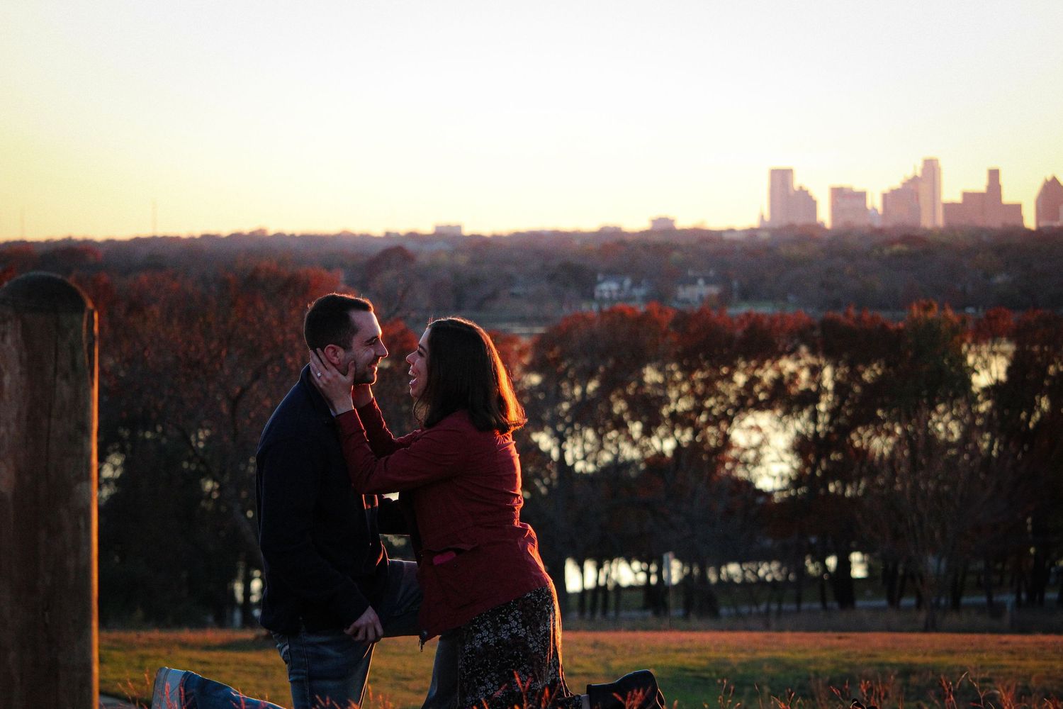 Romantic sunset proposal with city skyline glowing in background.