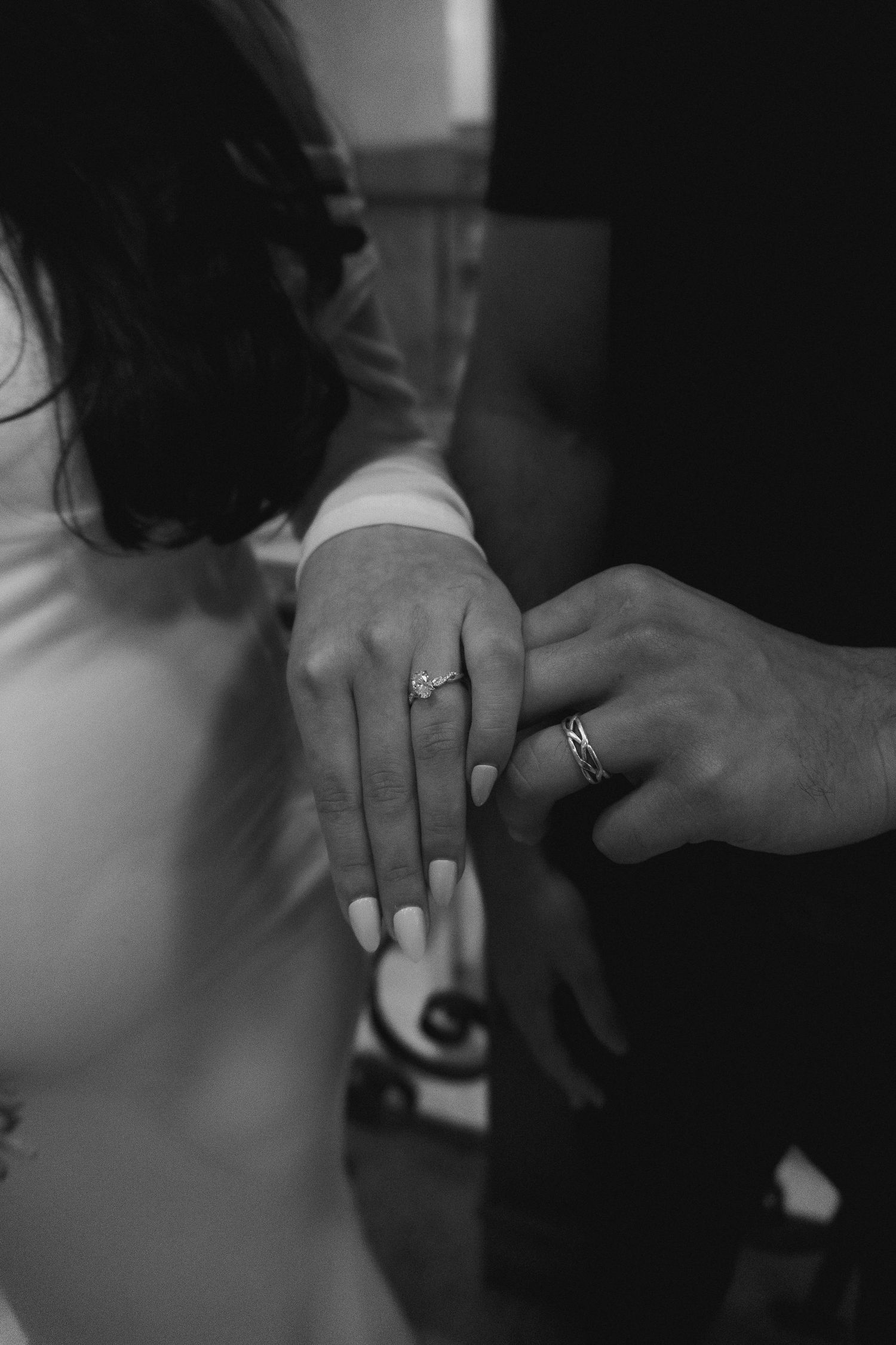 Black and white close-up photo showing hands wearing wedding rings in a romantic gesture.