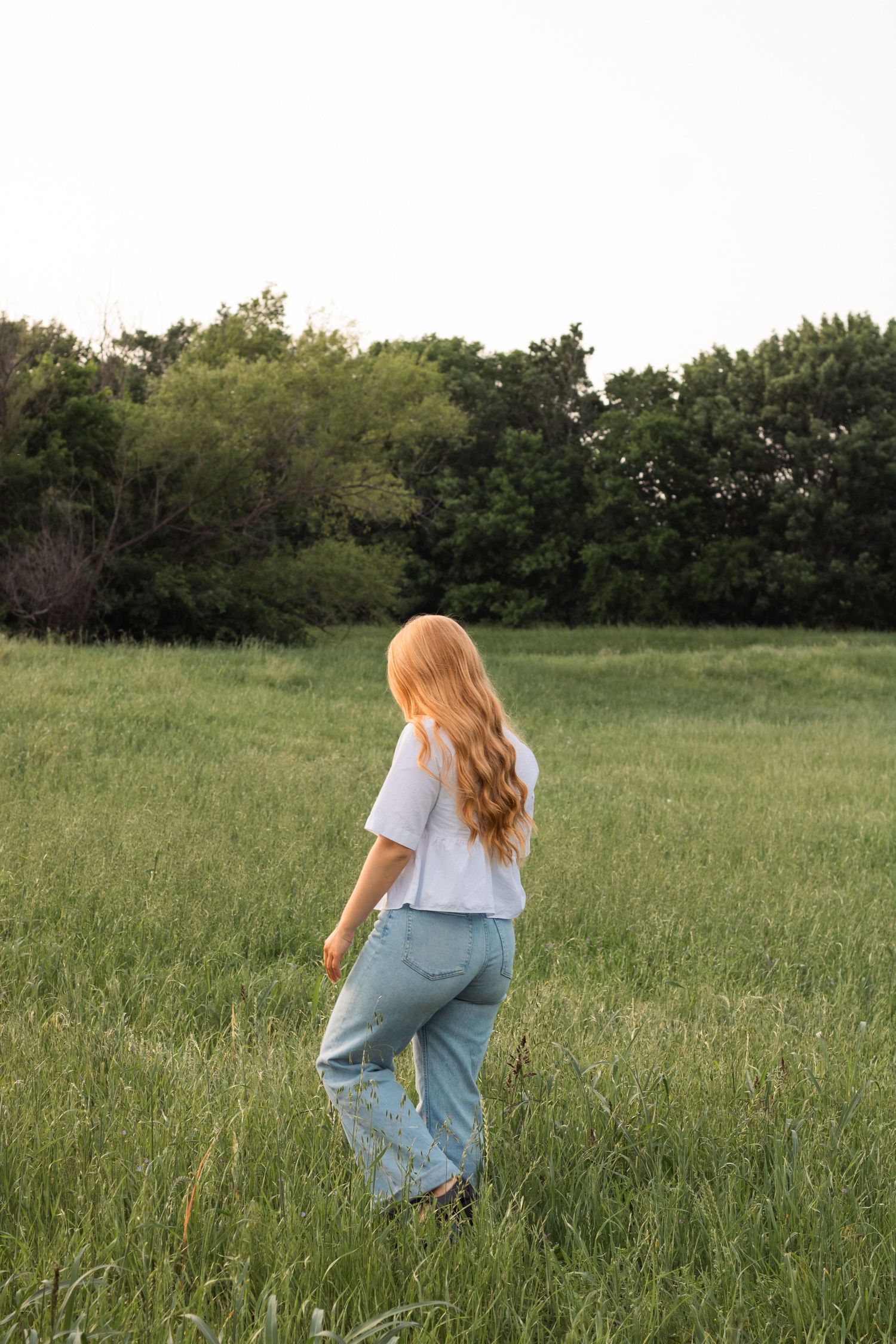Figure walking through tall grass in a field during golden hour.