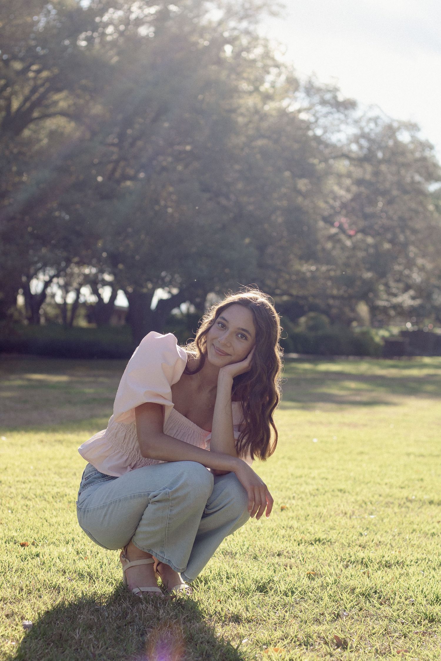 Person in casual attire crouching in a sunlit grassy field.