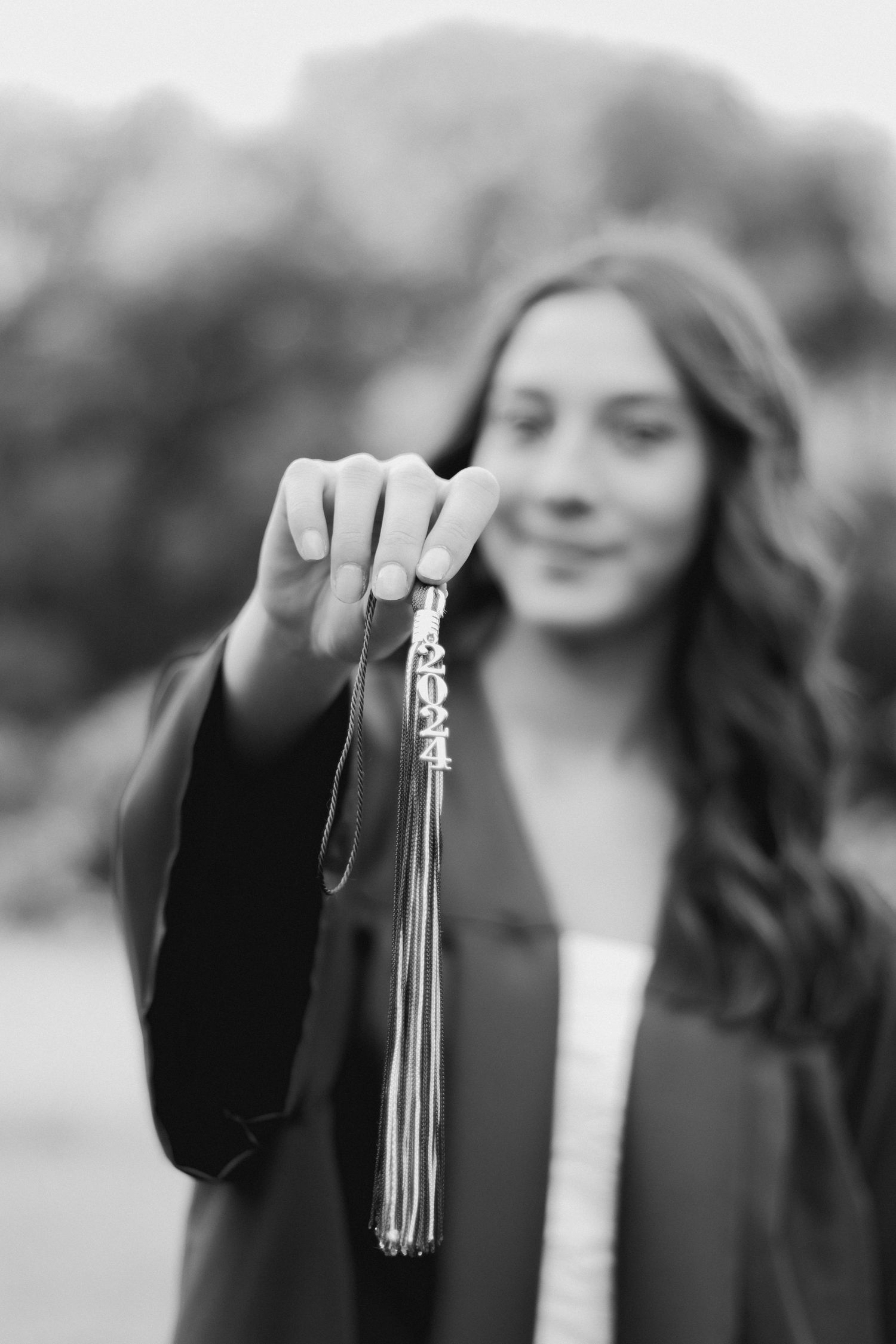 A graduate holds up their graduation tassel in a black and white photo with soft bokeh background.