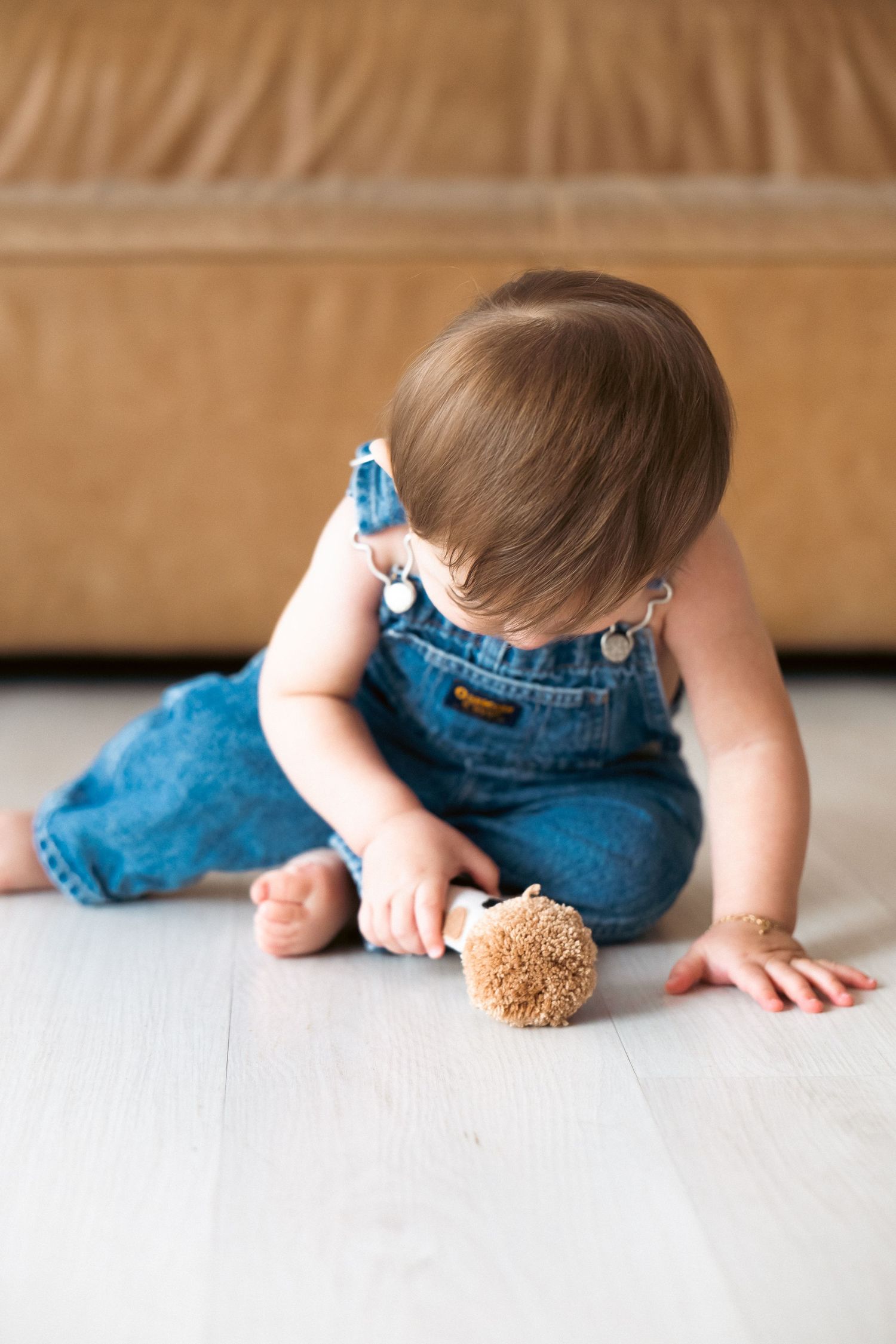 A small child in blue denim overalls crawls and explores on a light-colored floor.