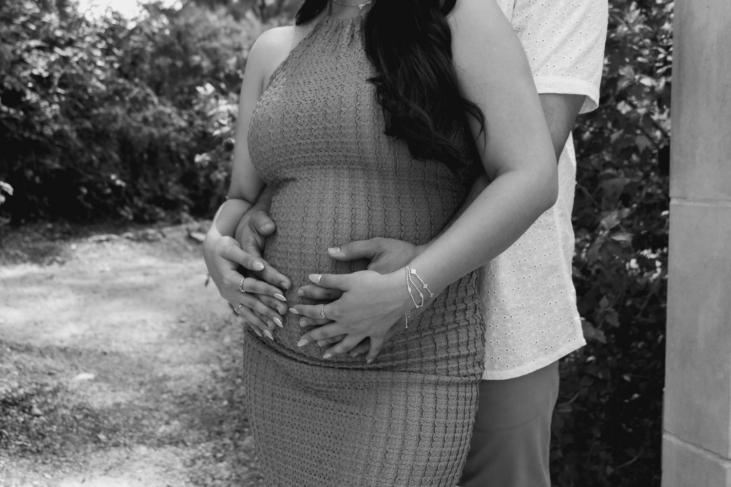 A black and white maternity photo session shows a couple embracing in nature, highlighting the pregnant belly.