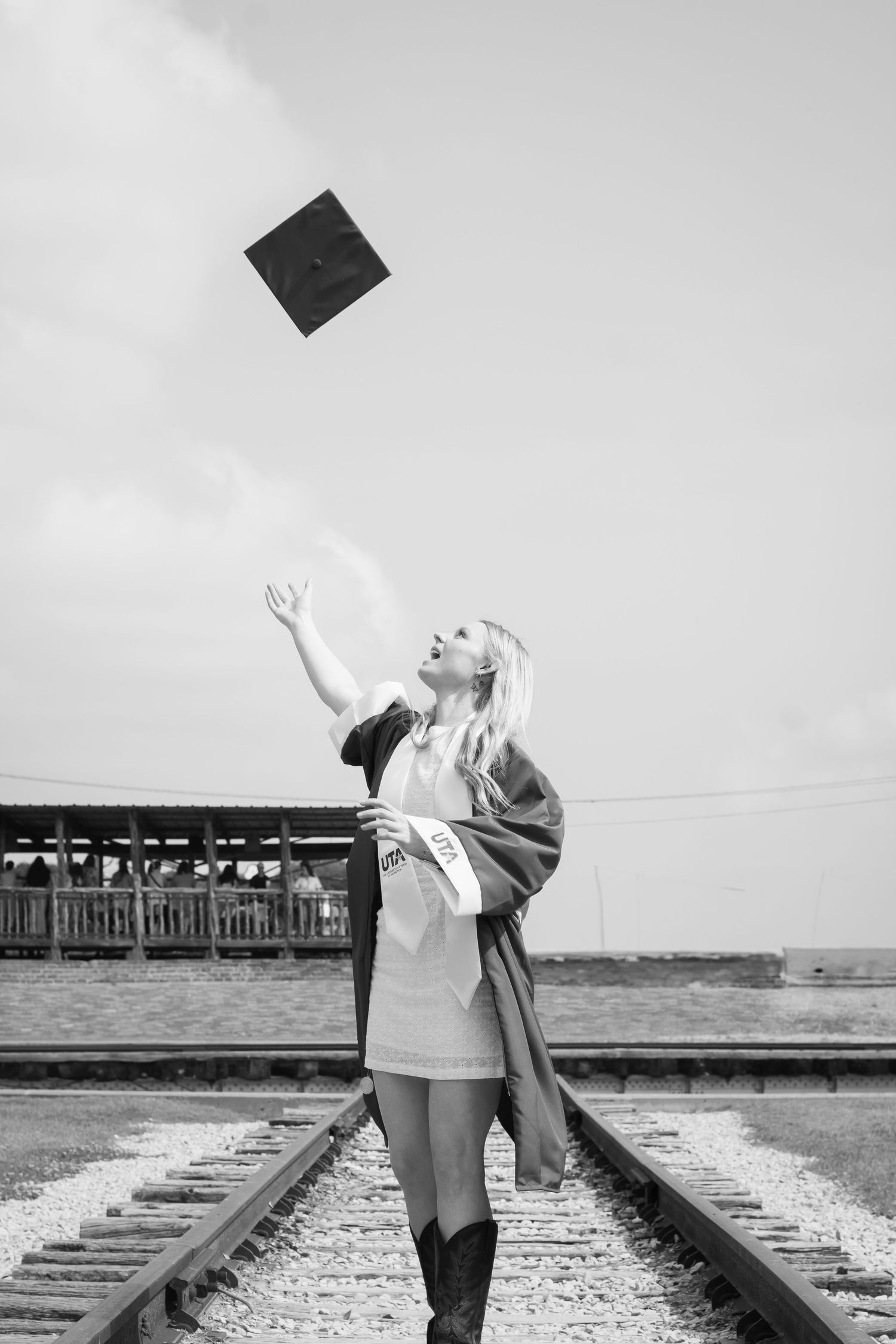 Black and white sequence of playful poses on railroad tracks with graduation cap being tossed.