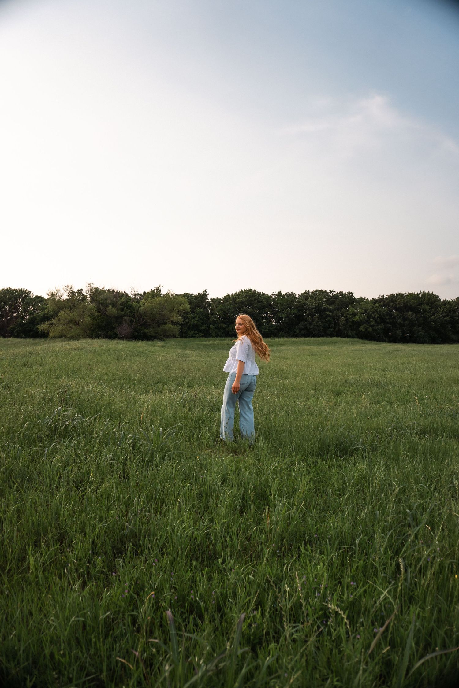 Person in white walking through a serene meadow with tall grass at sunset.