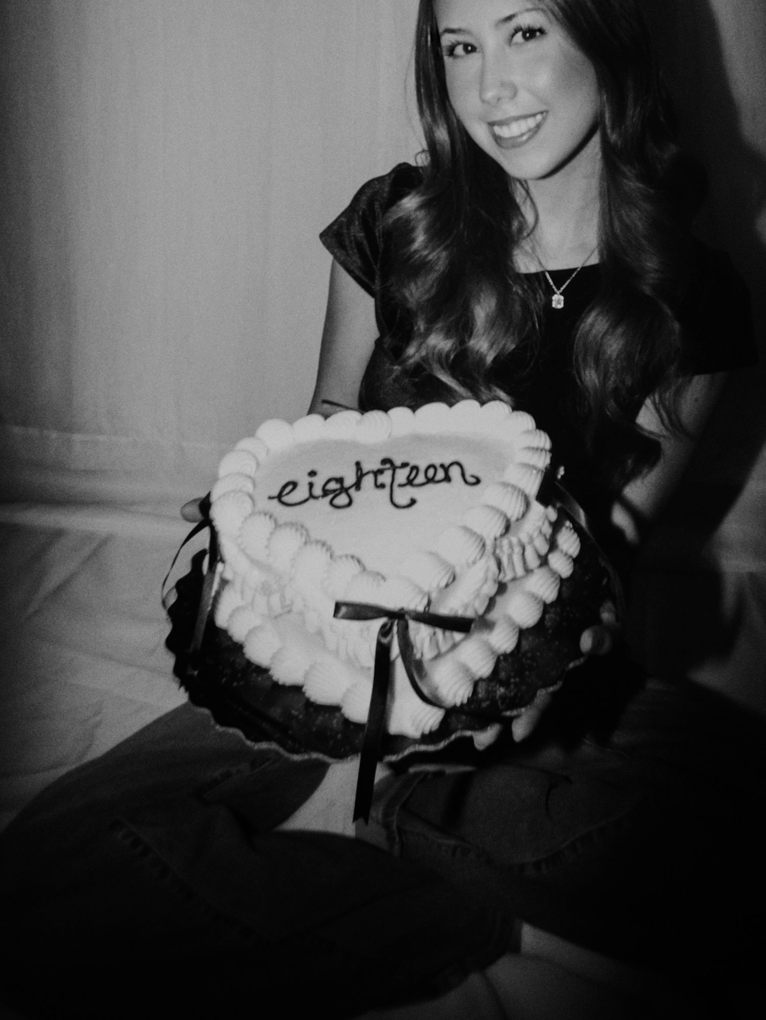 A black and white photo shows someone holding a decorative heart-shaped pillow with text embroidered on it.