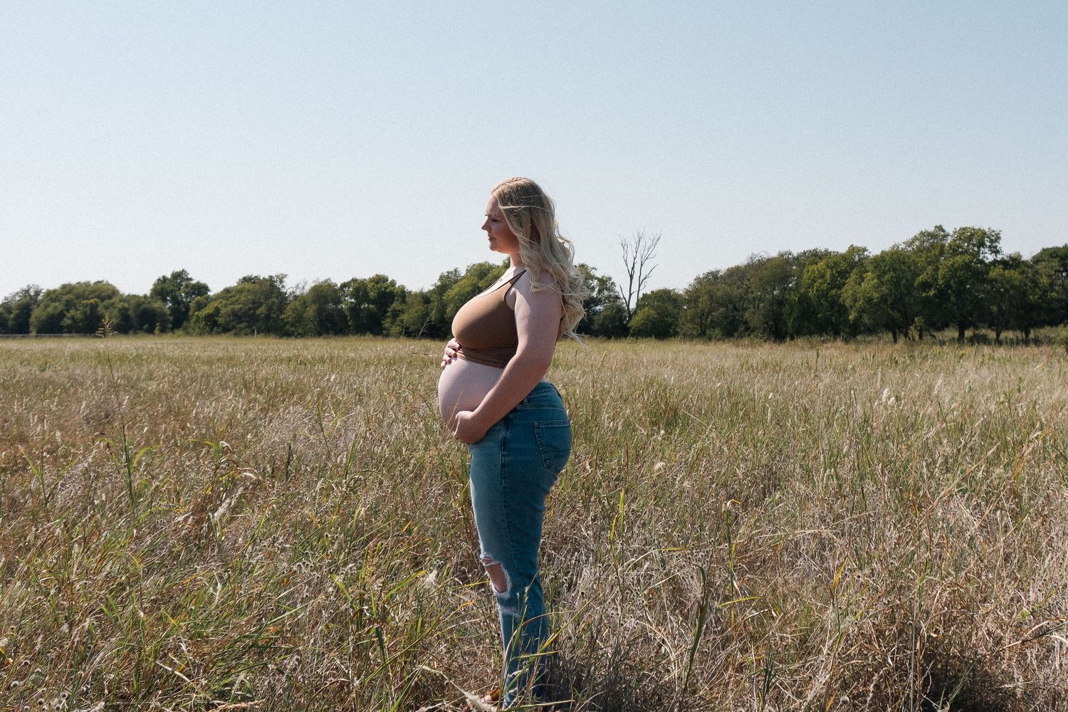 Expectant mother standing in sunny field during golden hour maternity shoot.