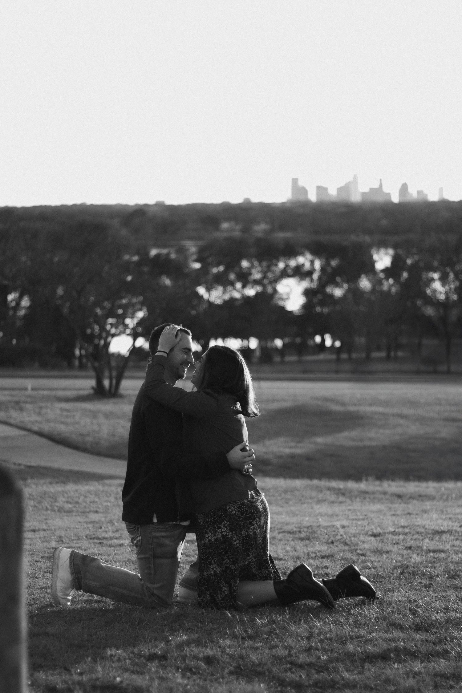 Couple sits together on hillside overlooking distant cityscape at golden hour.