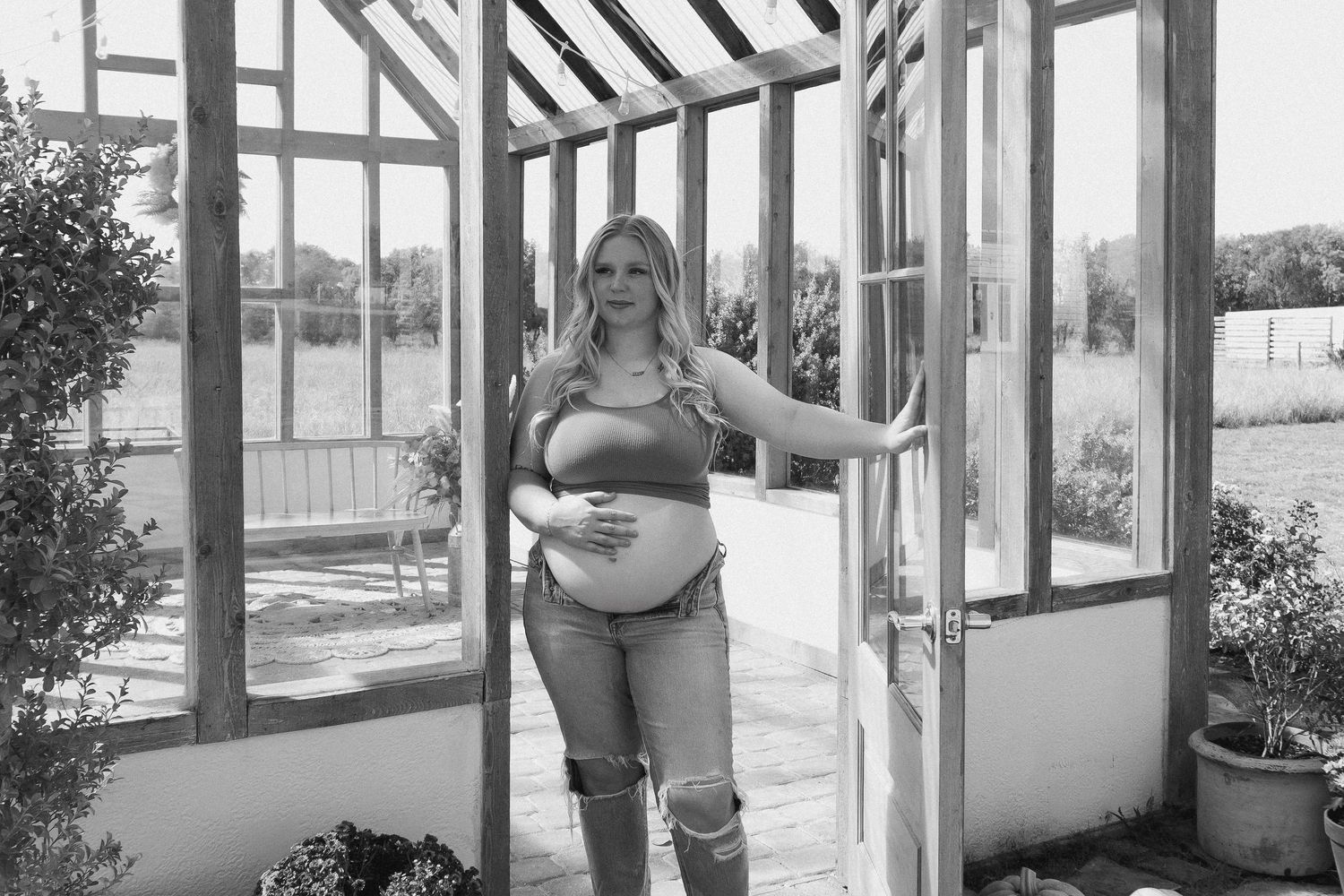 Maternity photo in greenhouse wearing casual clothes with natural lighting.