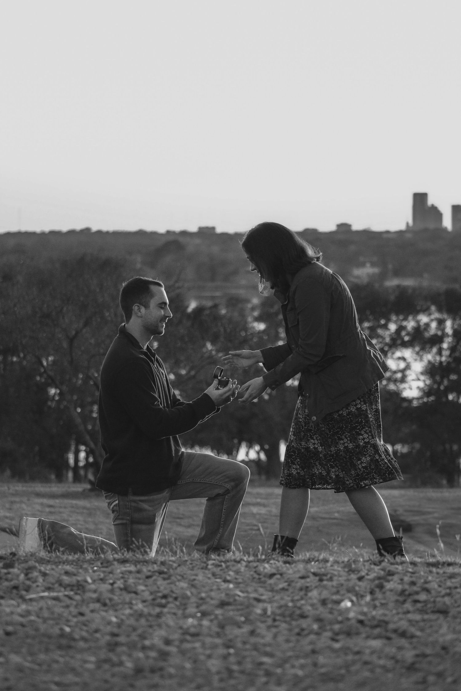 Romantic silhouette of a proposal scene at sunset with a city backdrop.