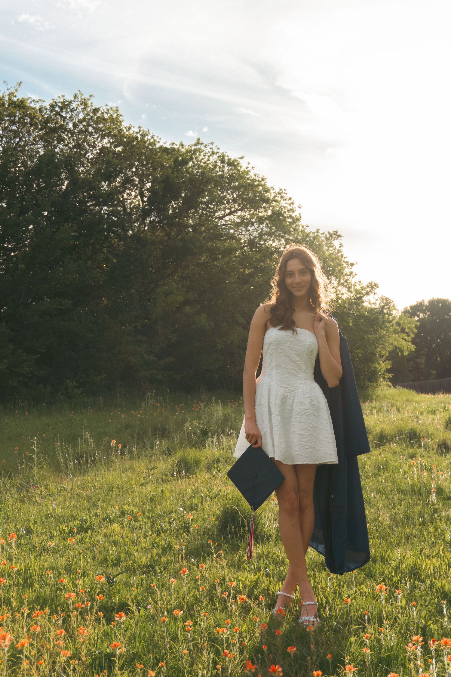 Person in white dress walking through a vibrant wildflower meadow at golden hour with trees in background.