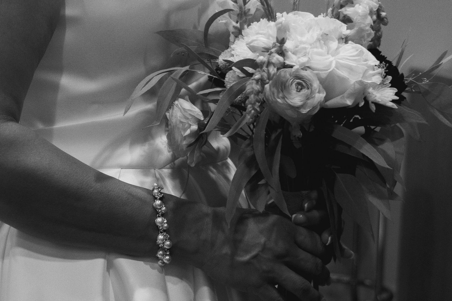 Close up detail shot of hands holding a white and blush wedding bouquet.