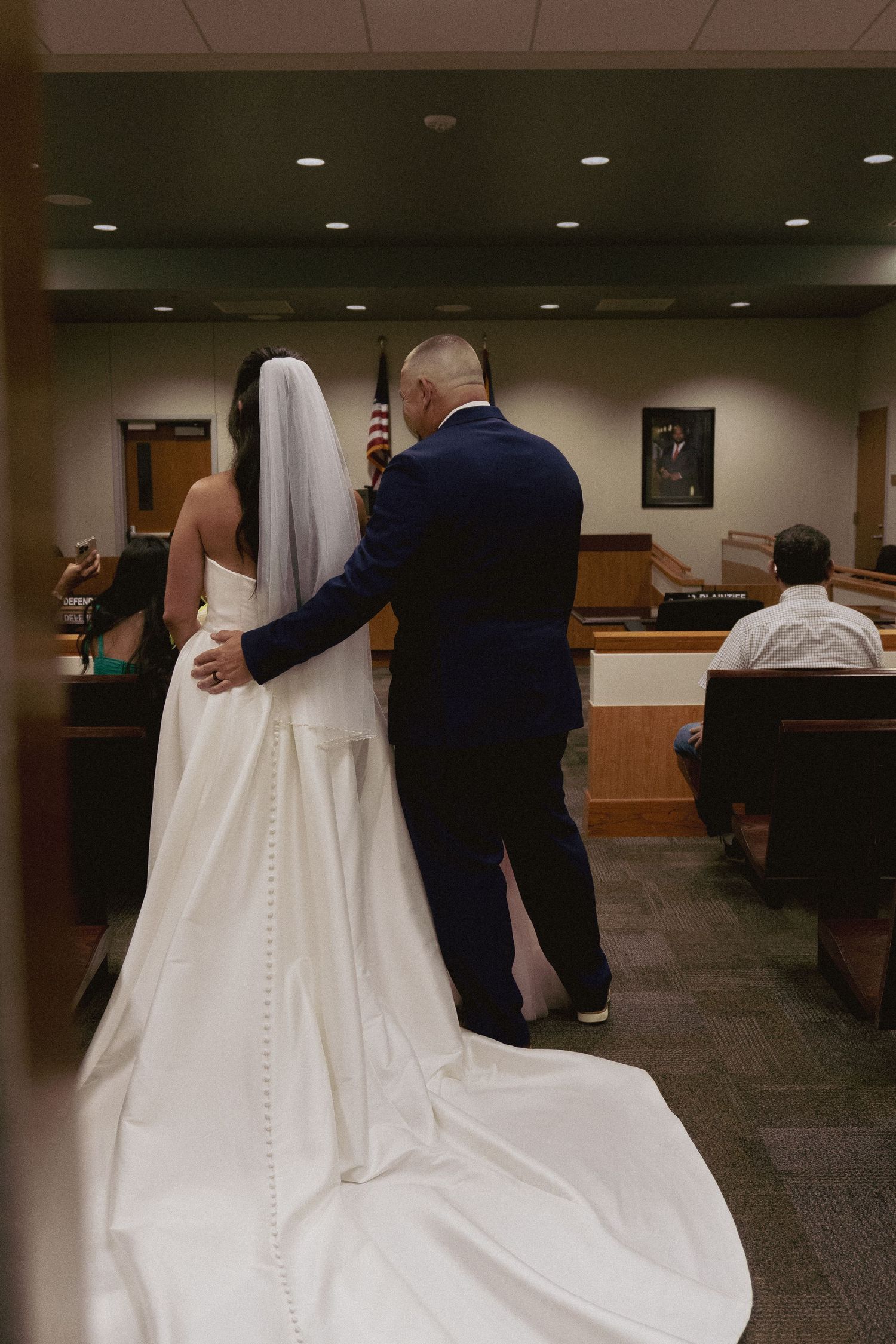 A view from behind of a couple in wedding attire standing in a courthouse.