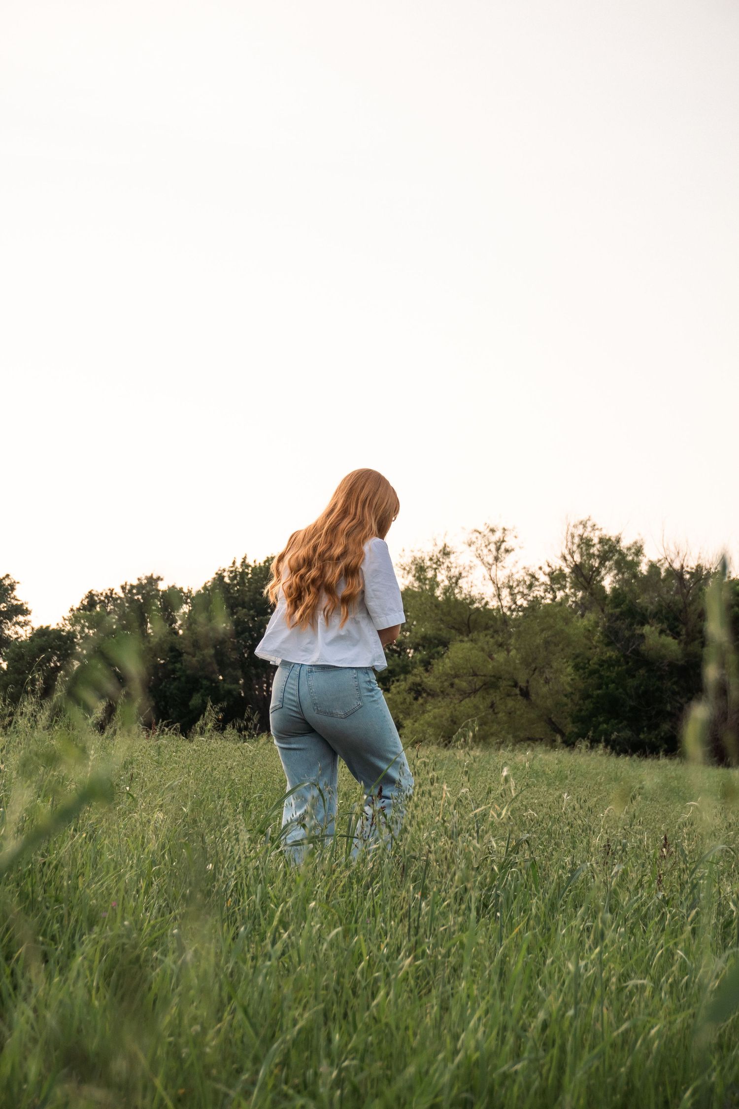 Individual strolling through a grassy field wearing jeans and a white top.