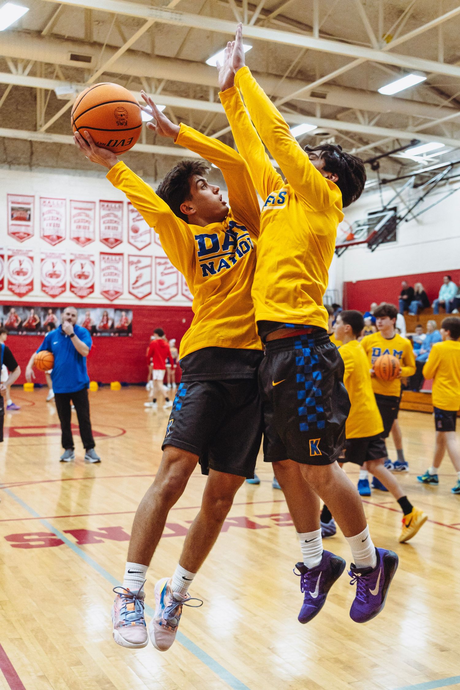 Two young basketball players in yellow jerseys jump for the ball during an indoor gym game.