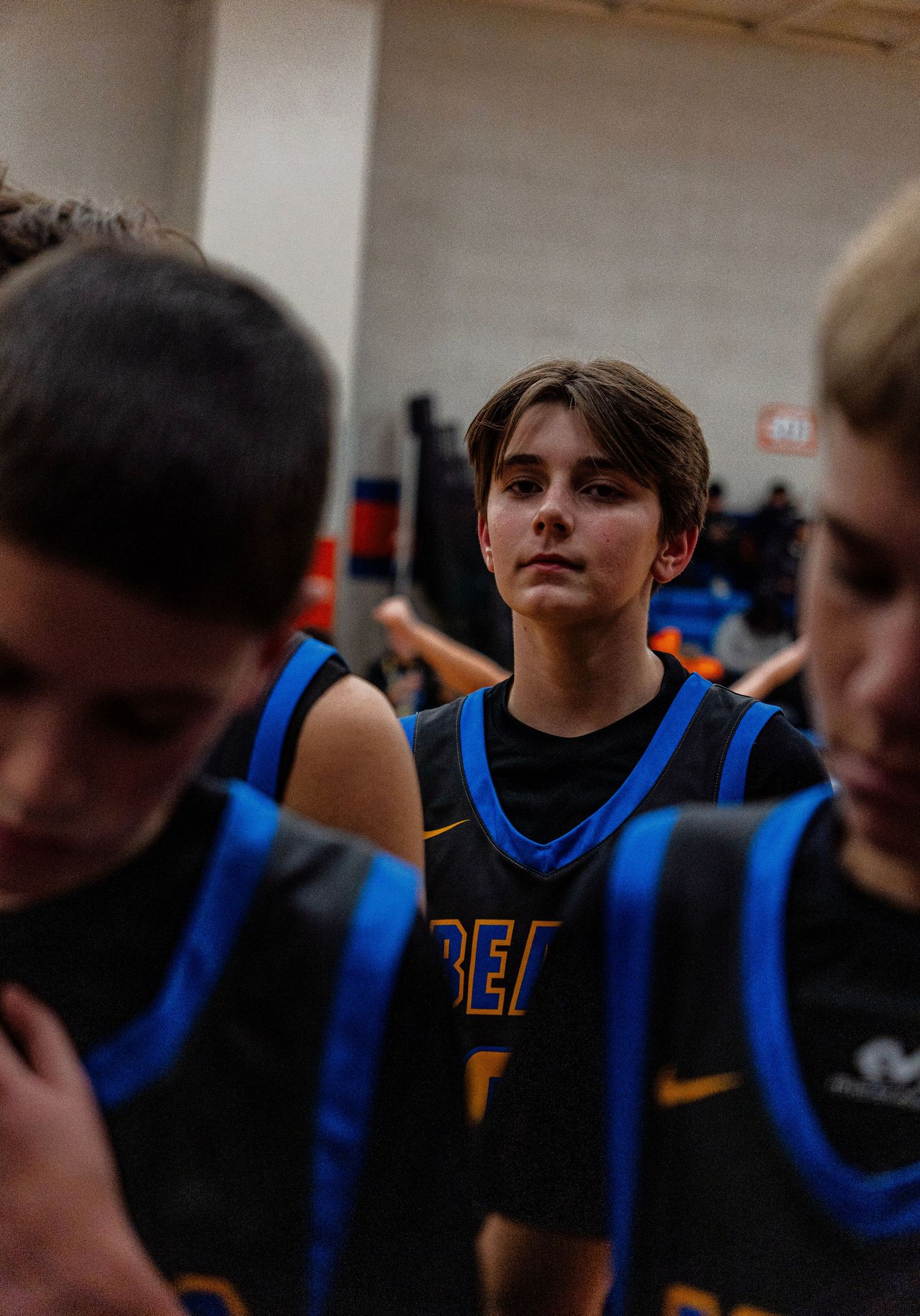 Young basketball player in Beavs uniform stands focused among teammates in a gym.