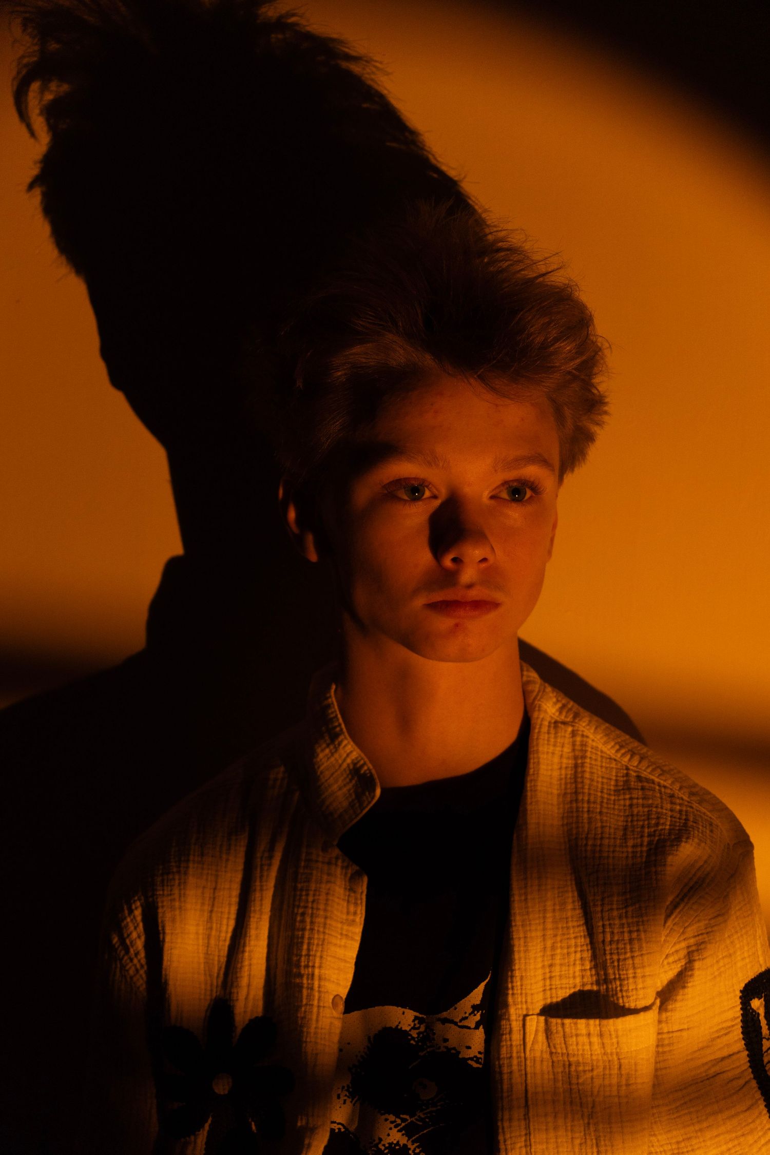 Moody orange-lit portrait of young man with dramatic hair shadow.