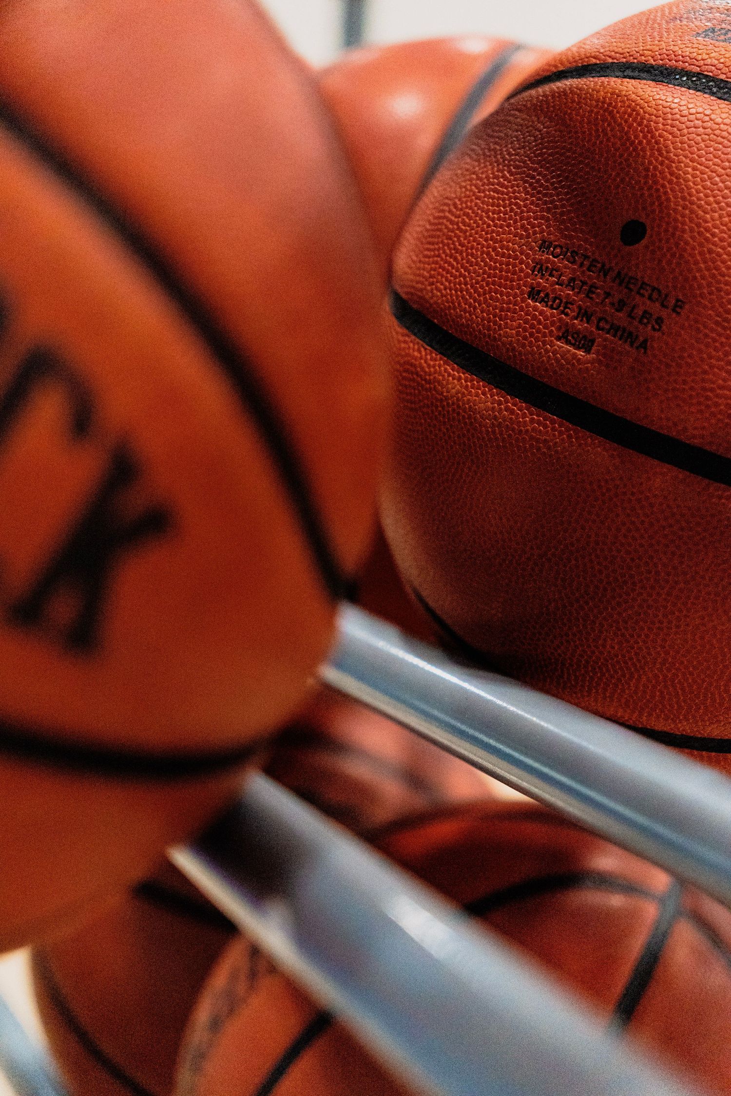 Close-up of multiple Wilson and Spalding basketballs stored in a metal rack ready for a game.