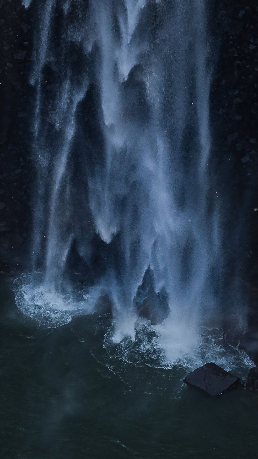 A powerful waterfall cascading down dark rocks into a turbulent pool of churning blue water.