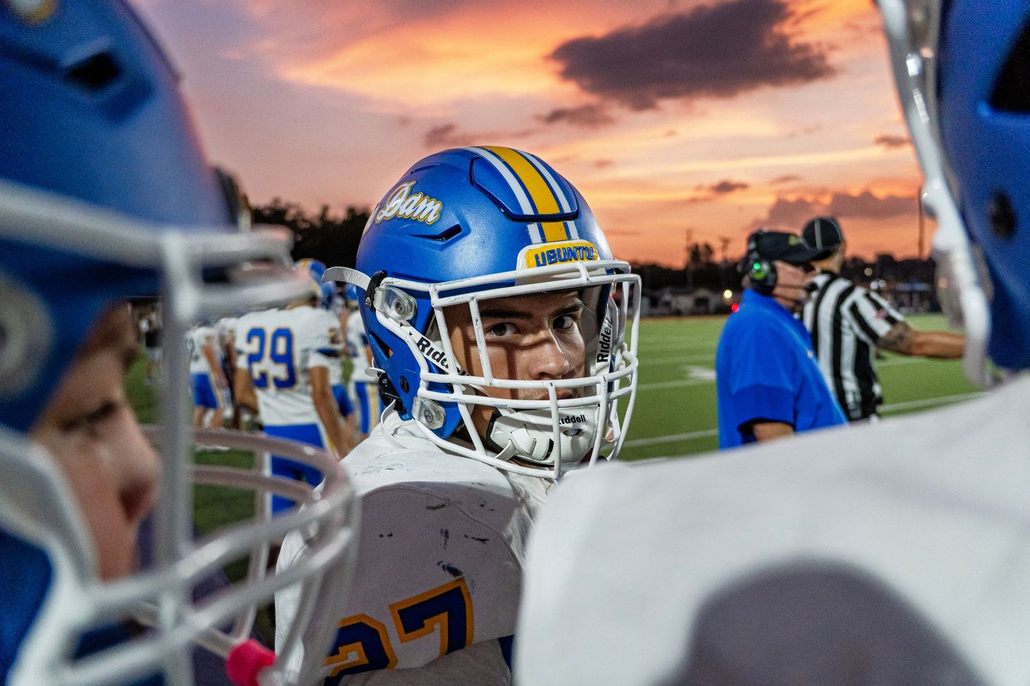 A Karns high school football player peers through helmets during a game at sunset.