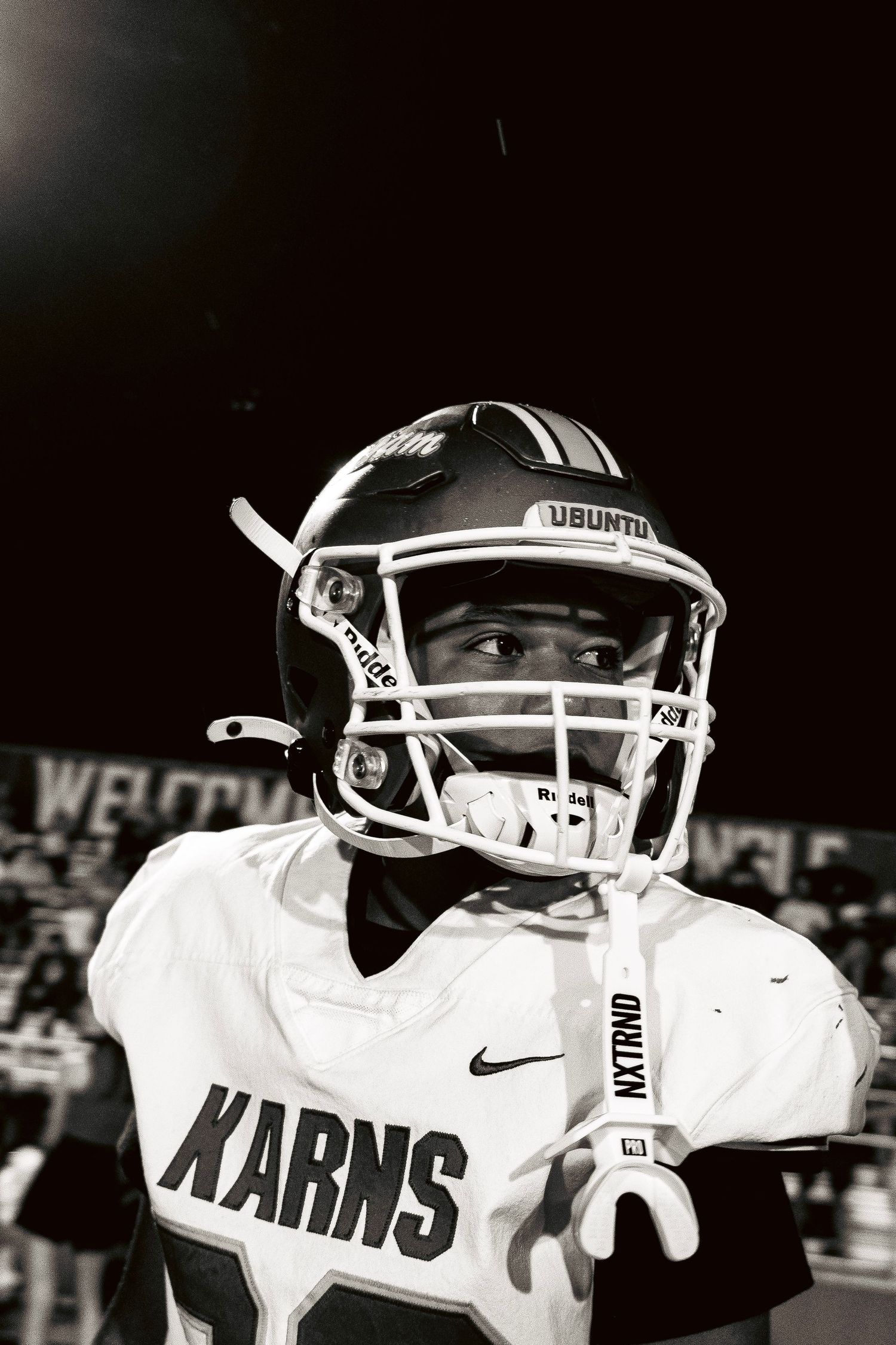 Black and white portrait of Karns football player in helmet and white jersey under stadium lights.