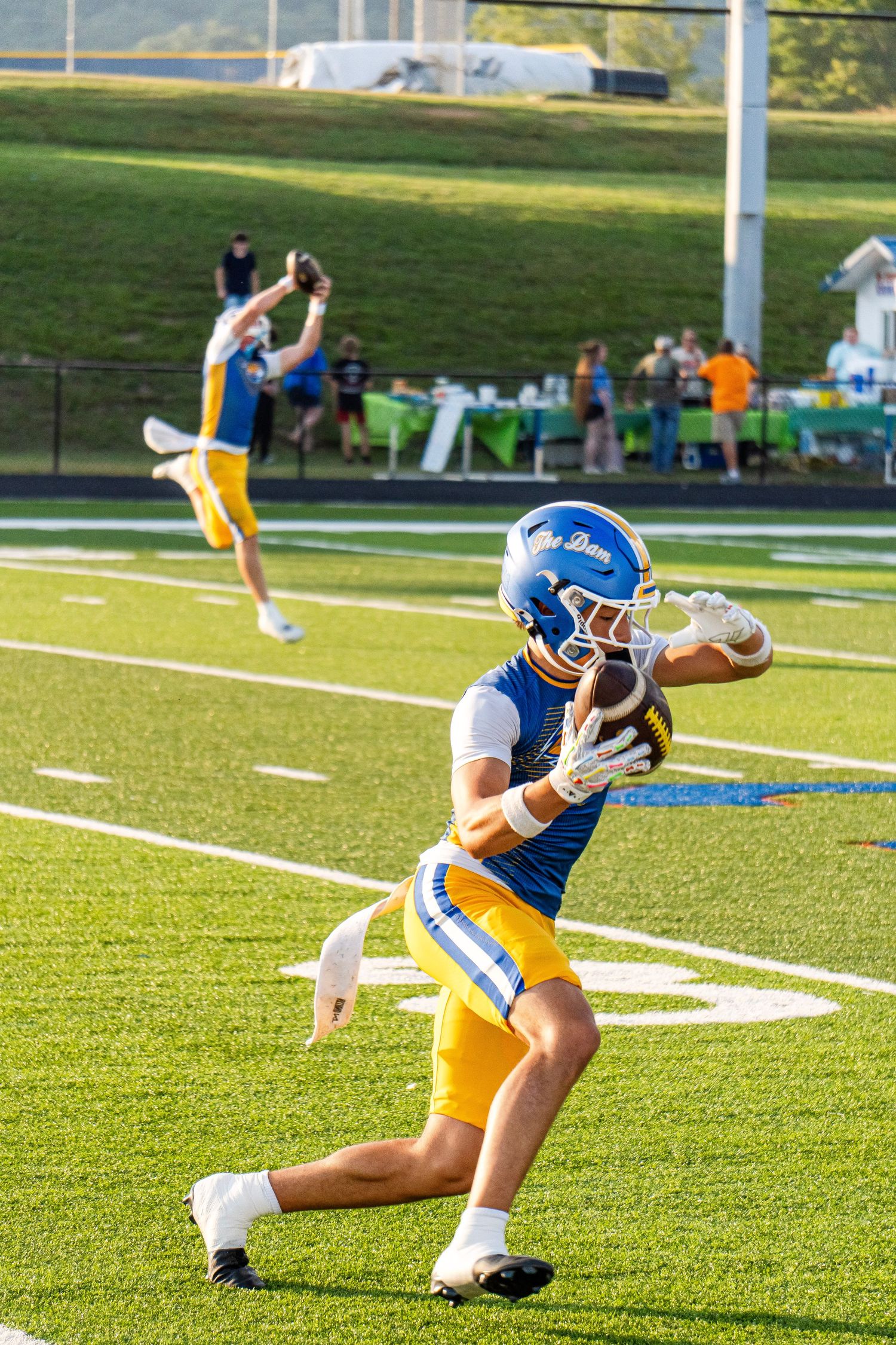 High school football player in blue and gold uniform catches a football during pre-game warmups.