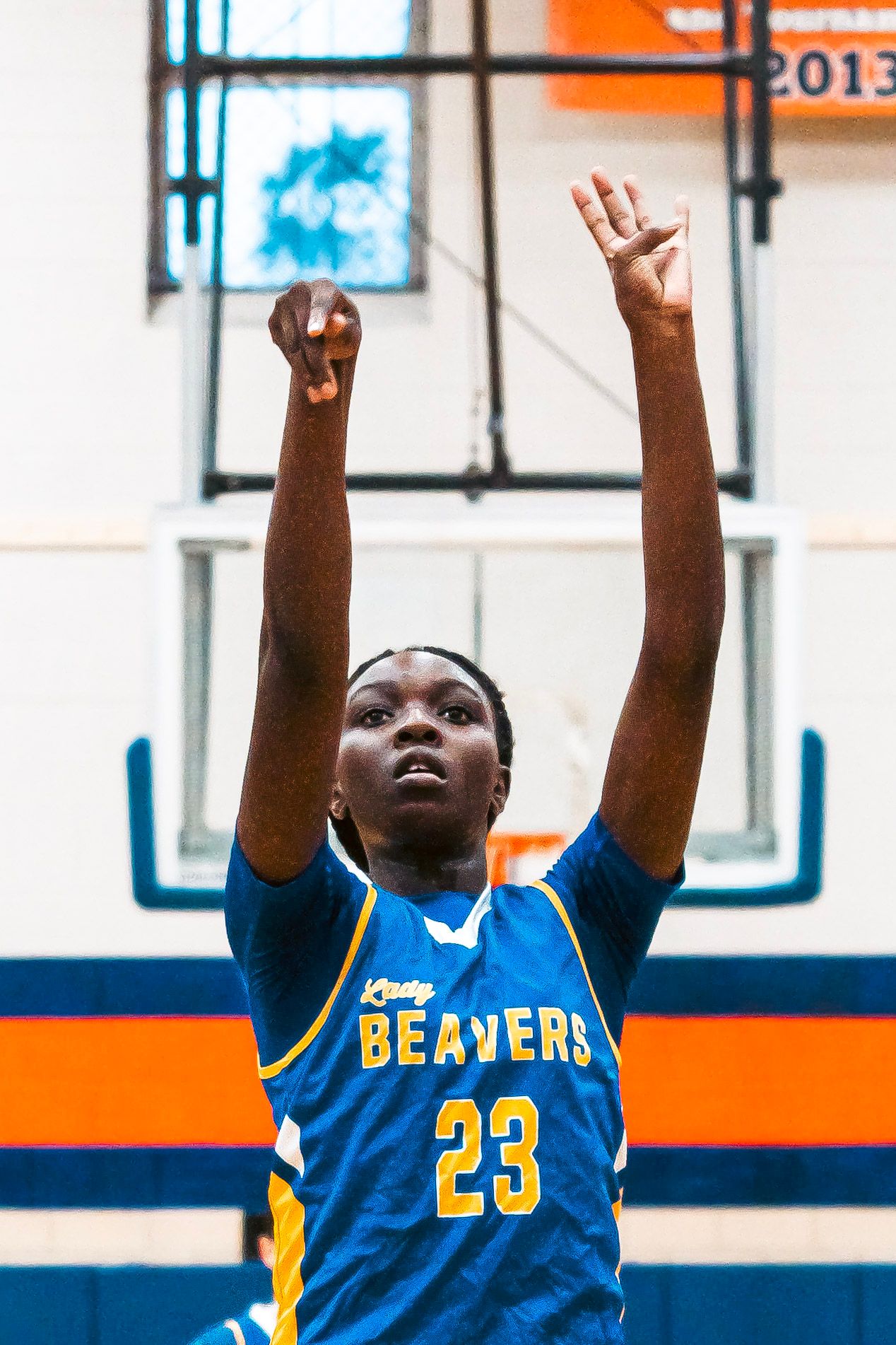 Female basketball player #23 in blue Beavers uniform shoots free throw with hands raised toward basket.