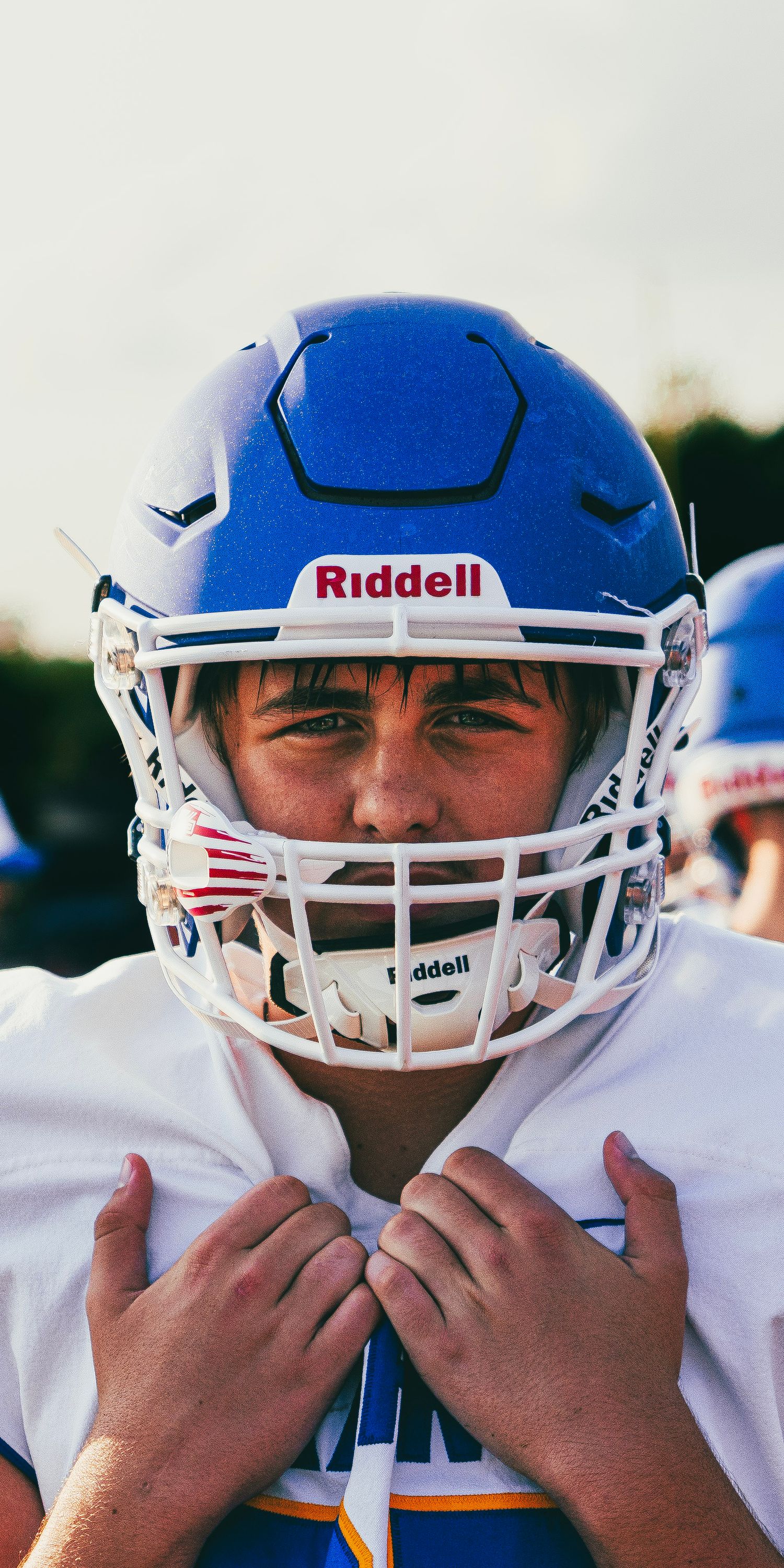 Young football player in blue Riddell helmet adjusts chin strap before game.