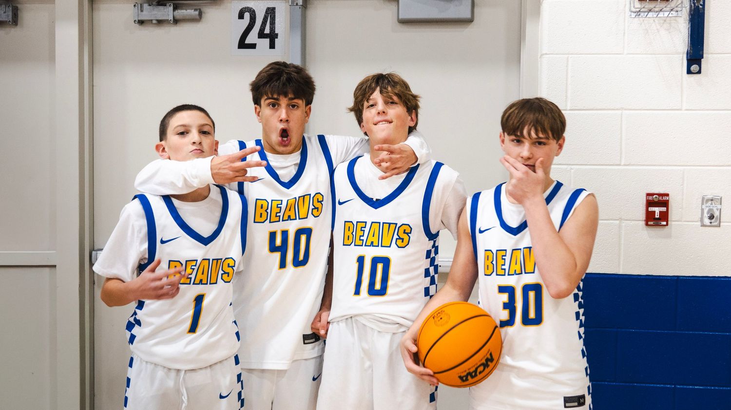 Four young basketball players in blue and white Beaus uniforms posing playfully in a gym.