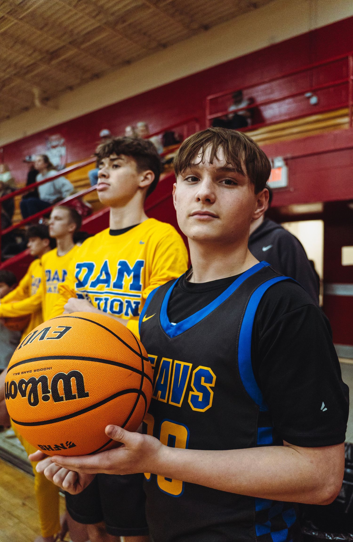 Young basketball player in blue Beavs jersey holding a Wilson ball with teammates in background.