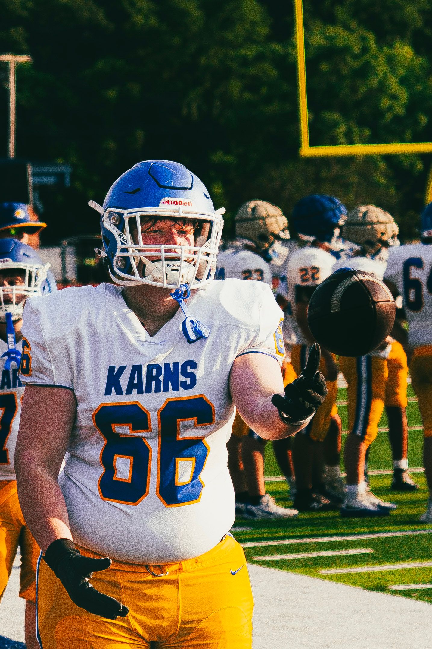 Karns football player number 66 in white and gold uniform holding a football on the sideline.