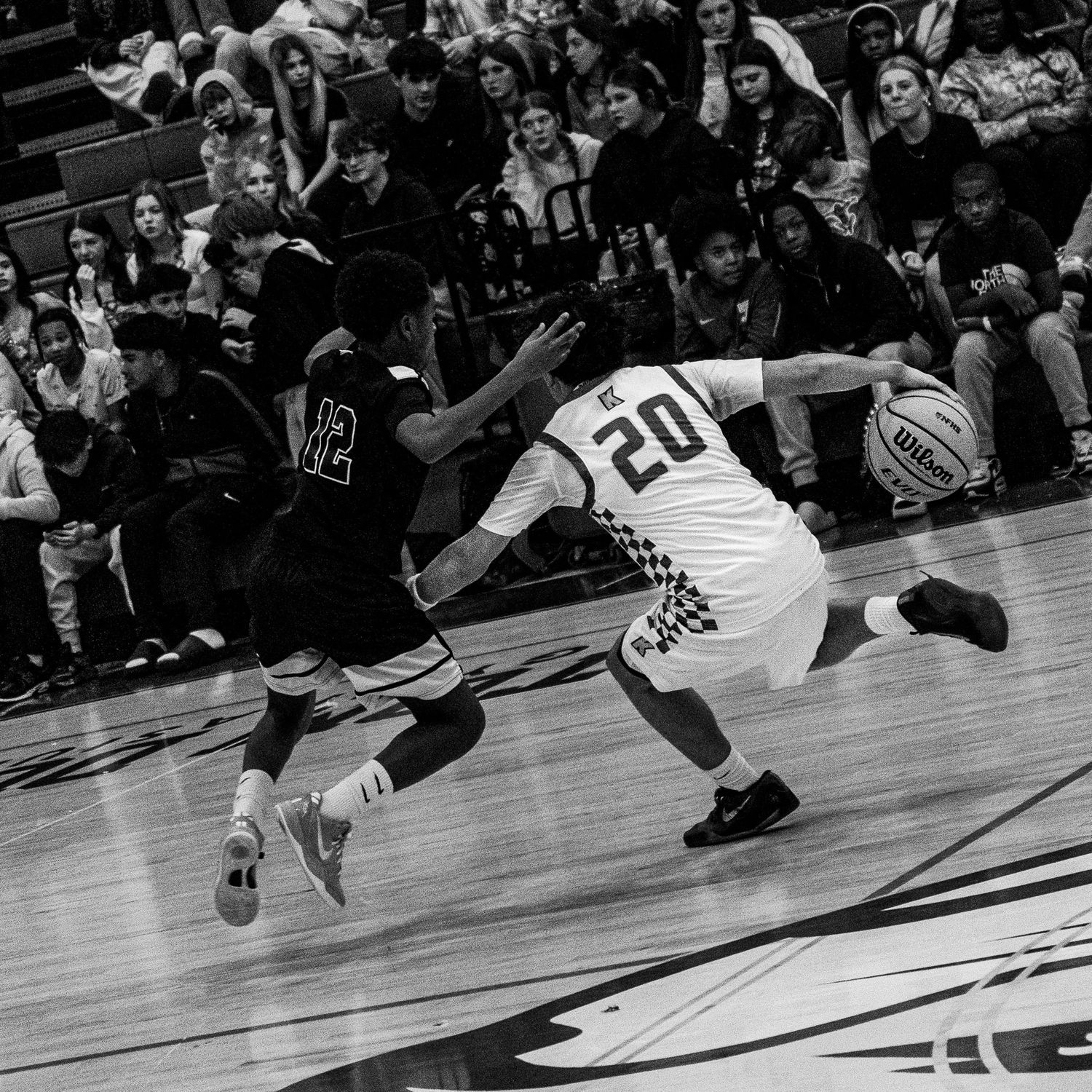 Black and white action shot of basketball player number 20 dribbling past a defender.