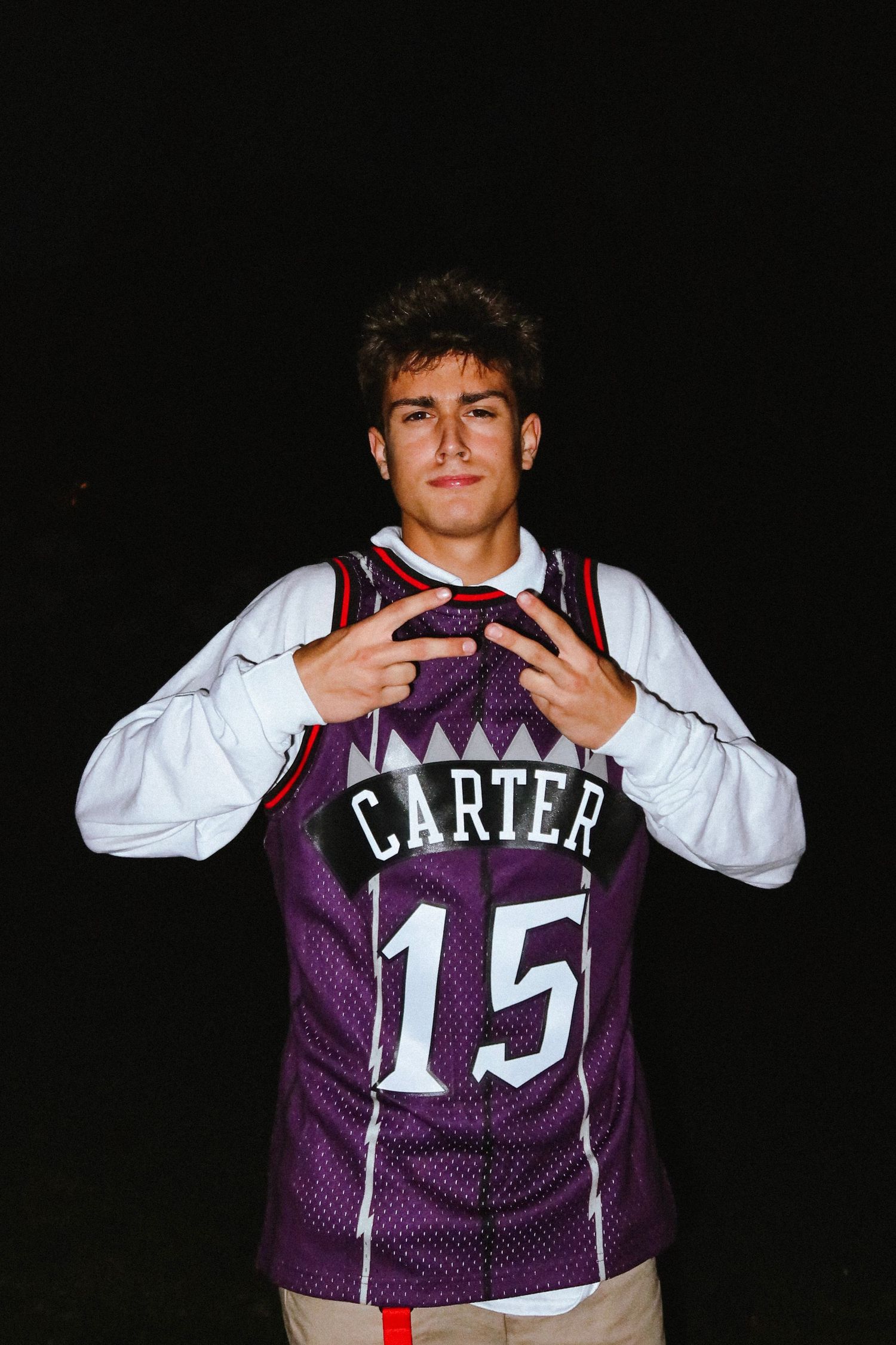 Young man posing outdoors at night wearing a purple Vince Carter #15 Toronto Raptors basketball jersey.
