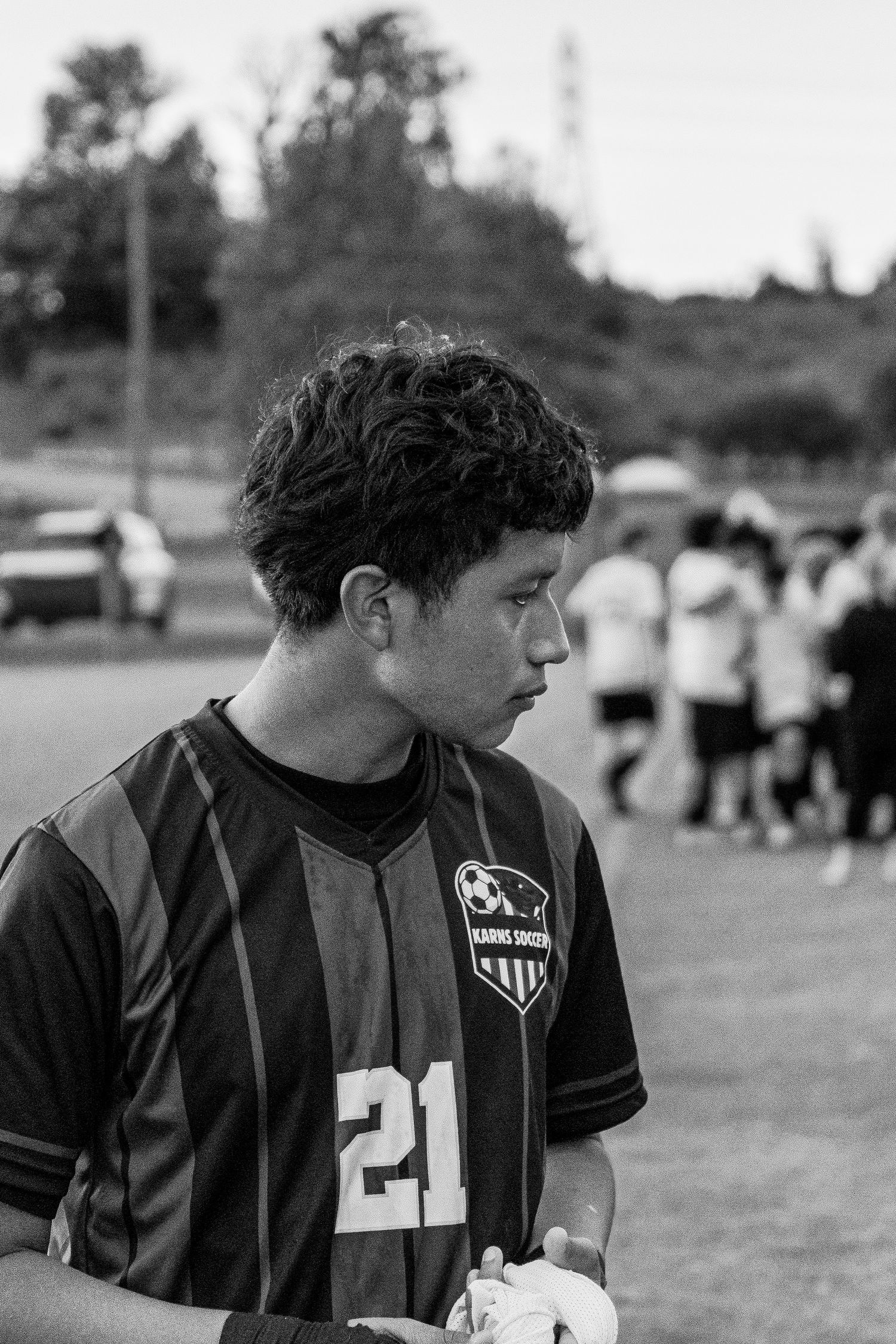 Black and white portrait of curly-haired teen soccer player #21 on field after game.