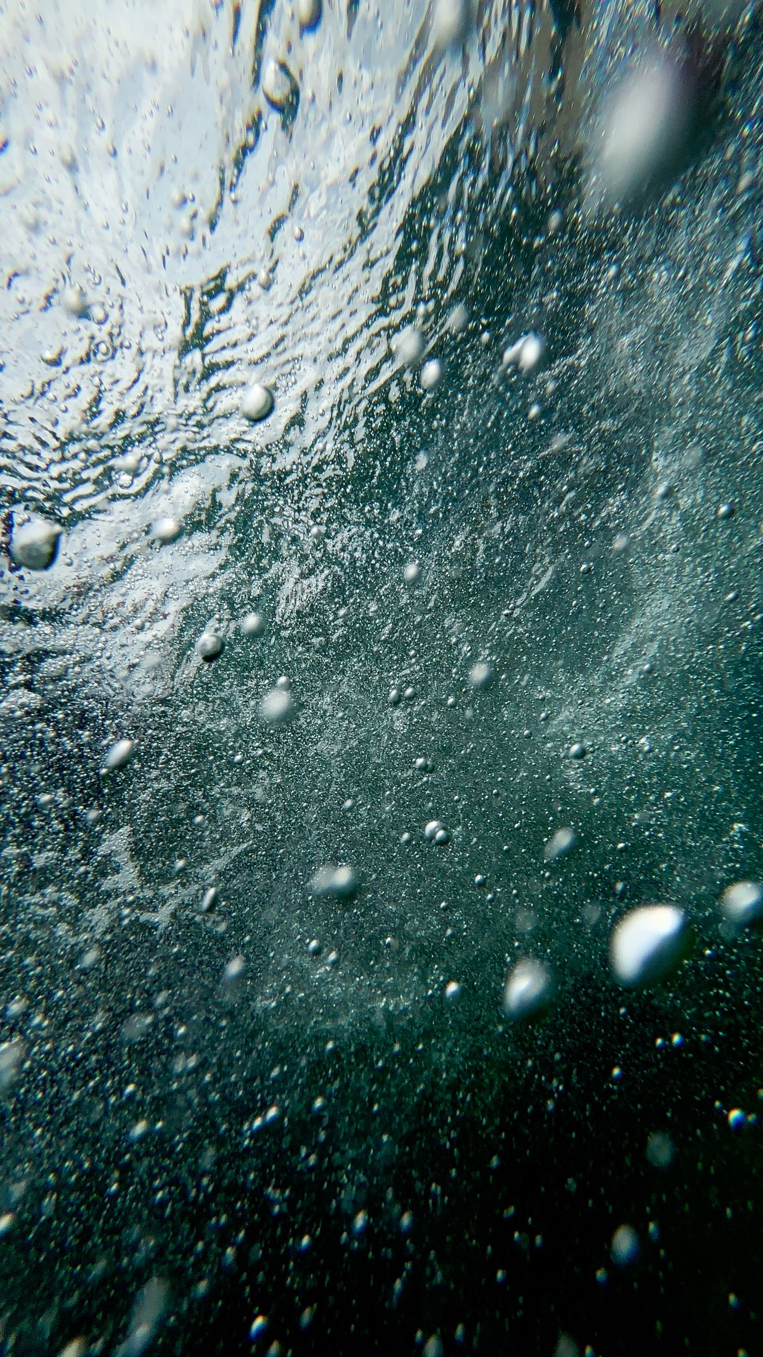 Underwater view of air bubbles rising through clear blue-green water toward the surface.