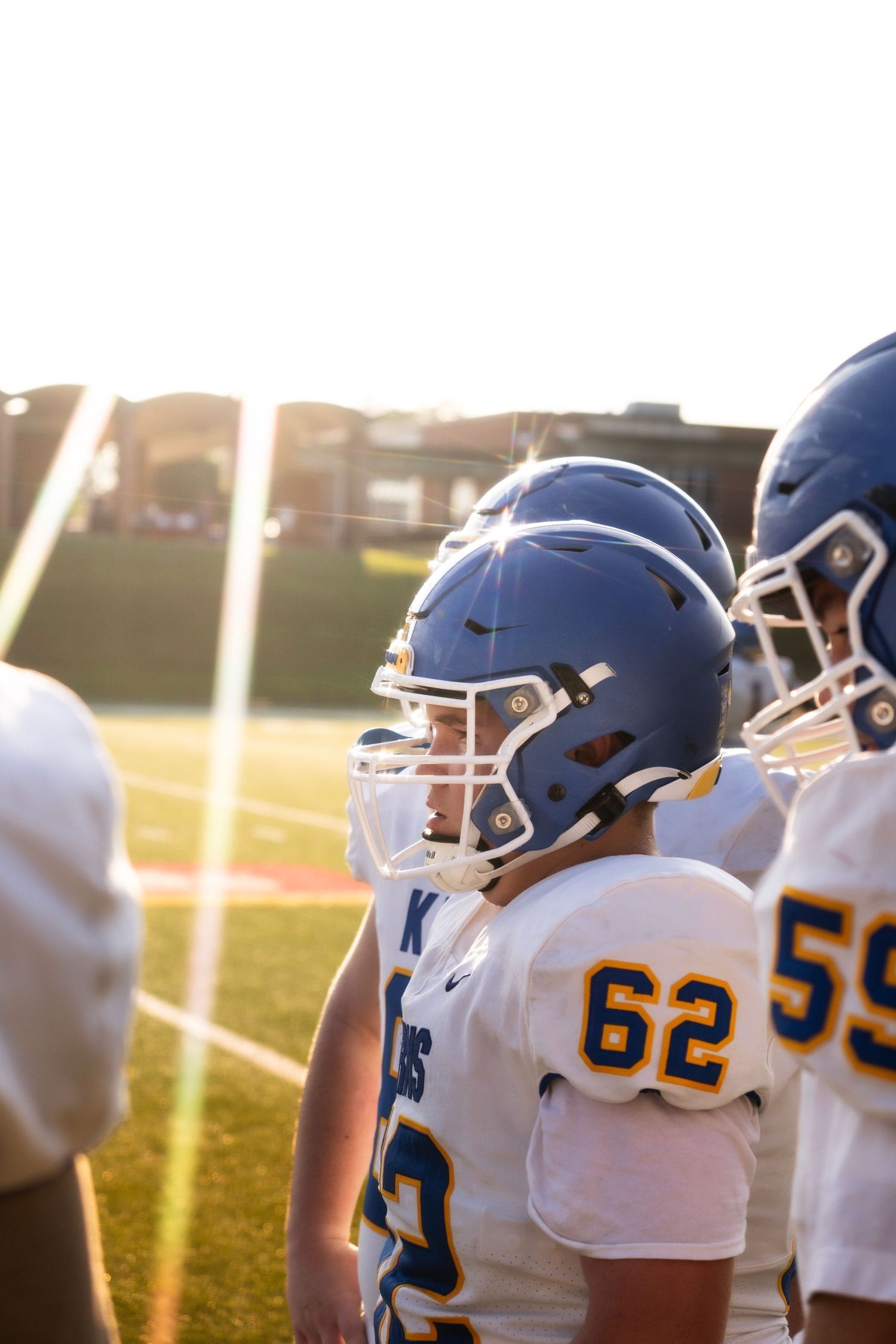 High school football players in blue and gold uniforms and helmets stand on the sideline during a game.