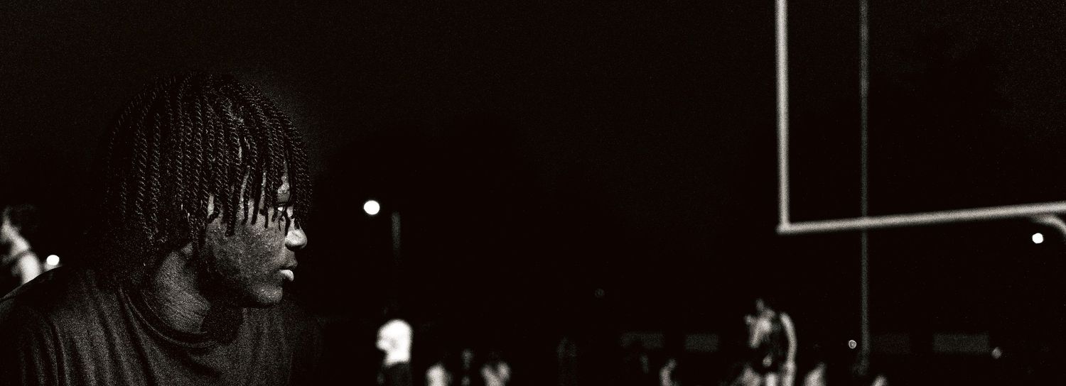 Black and white photo of a young athlete standing on a dark sports field at night.
