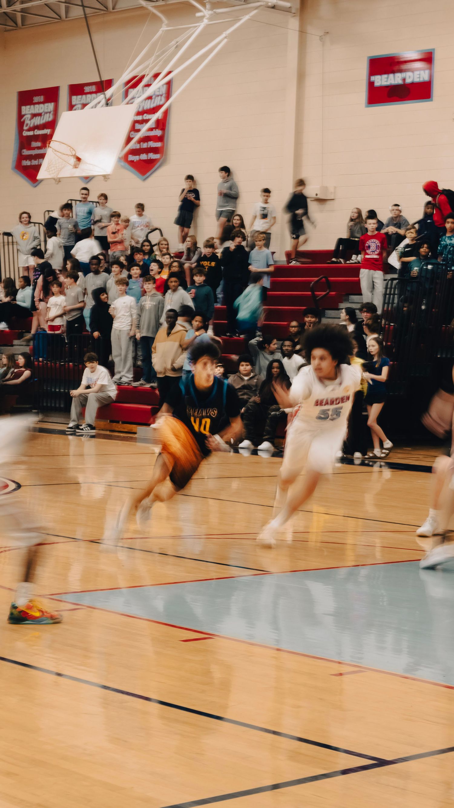 A basketball player in a teal jersey dribbles past a defender during a high school gym game.