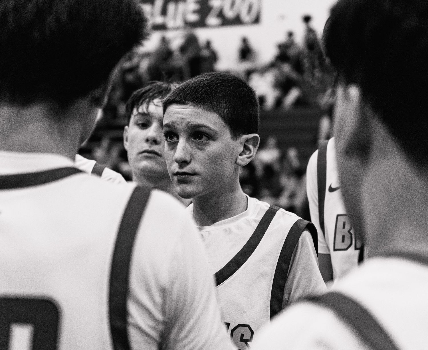 Black and white photo of focused young basketball player listening during team huddle in gym.