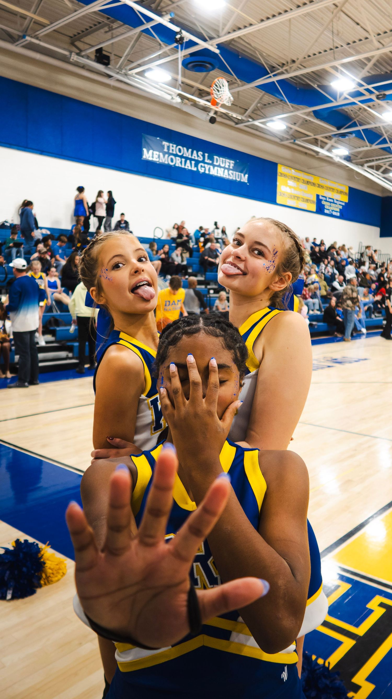 Three cheerleaders in blue and gold uniforms pose playfully at Thomas L. Duff Memorial Gymnasium.