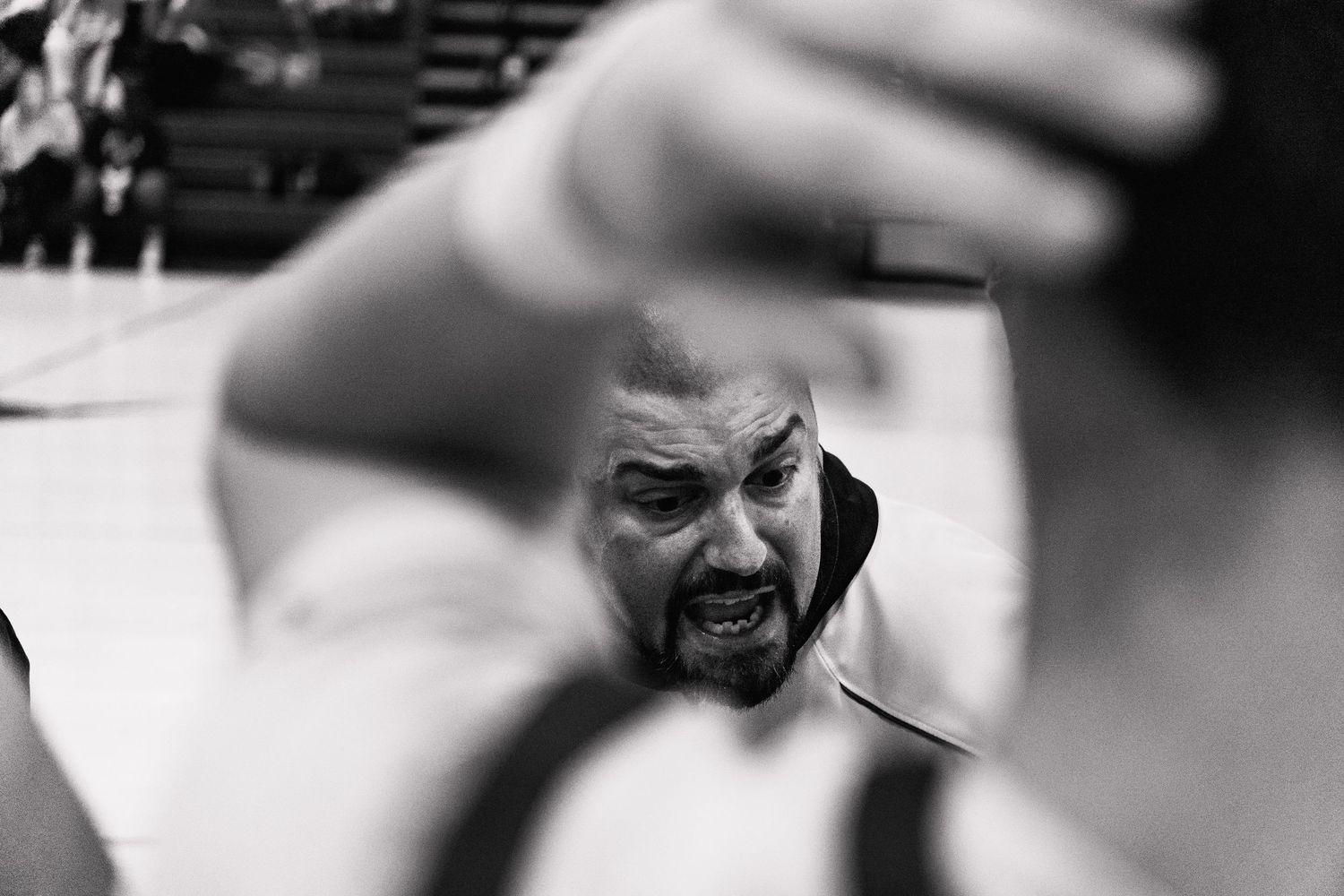 Black and white close-up of intense male basketball coach giving animated sideline instructions.