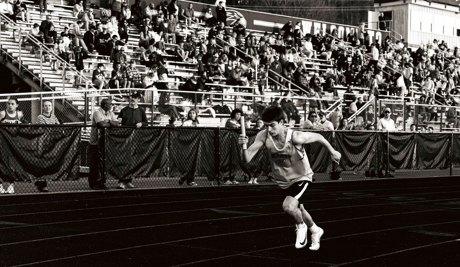 A track and field athlete in starting stance on a dark track with crowded bleachers in background.